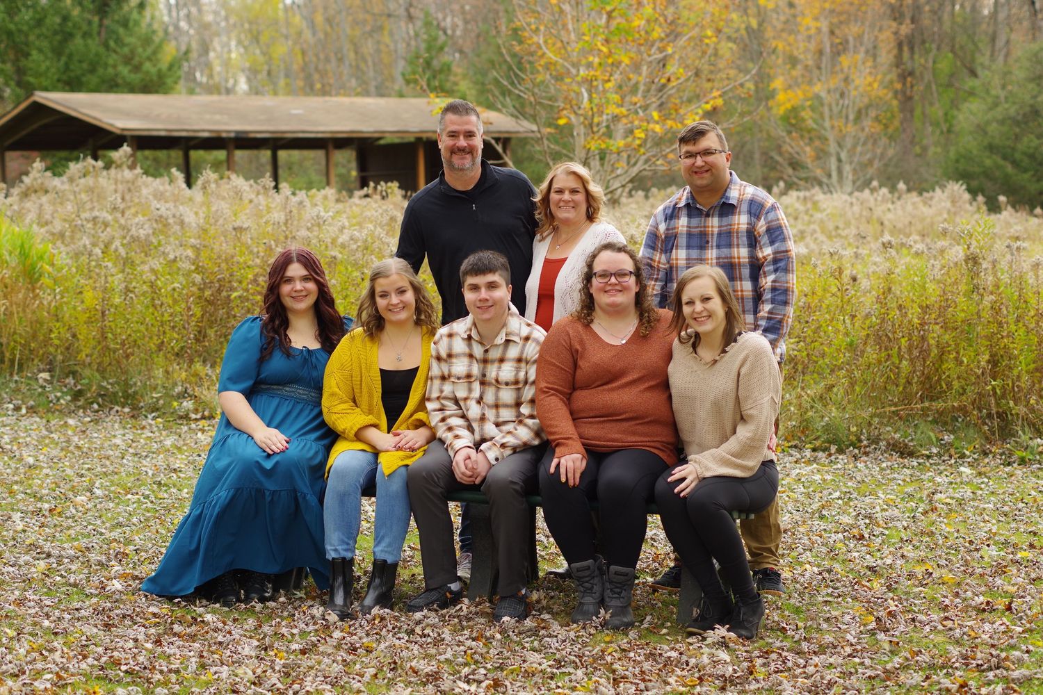 Family group portrait in natural setting with tall grass and autumn colors.