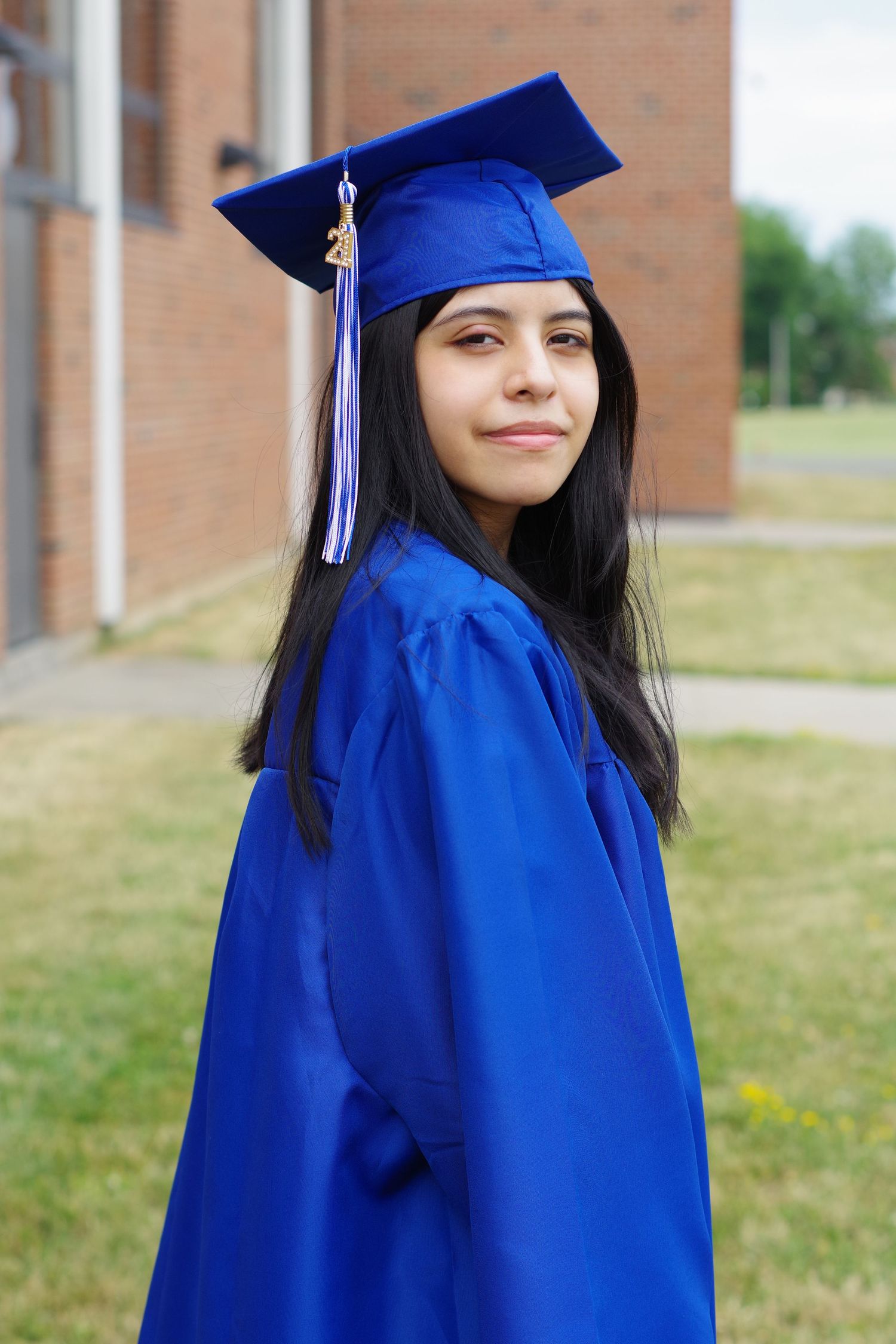 Graduate poses with confident smile in royal blue graduation attire against brick building.