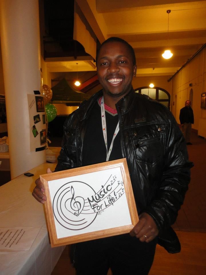 People posing with framed music-themed artwork in a warmly lit indoor space.