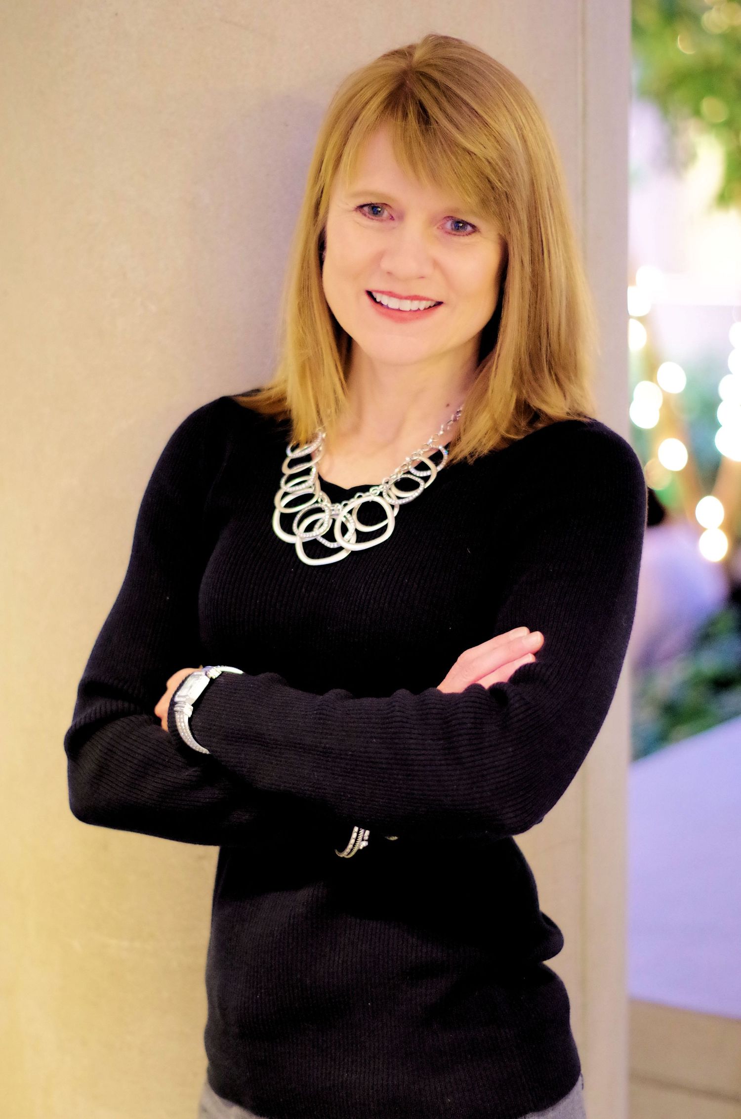 Professional studio portrait in black sweater with silver circle necklace and arms crossed.