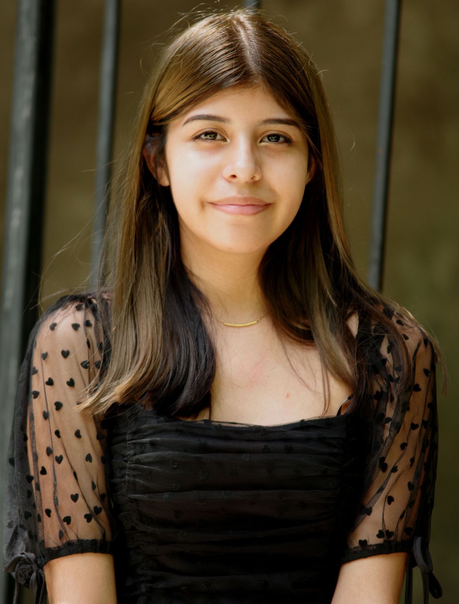A portrait in a black dress with sheer polka dot sleeves against a dark background.