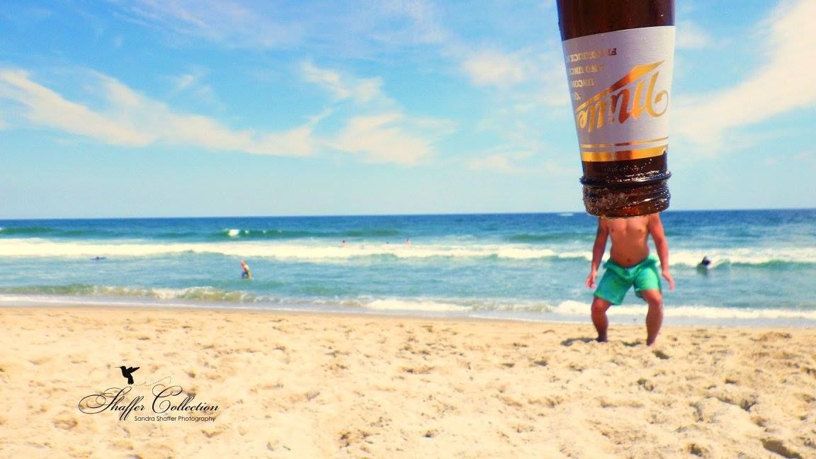 Beach scene with person doing handstand photographed to appear inside an upturned beverage container.