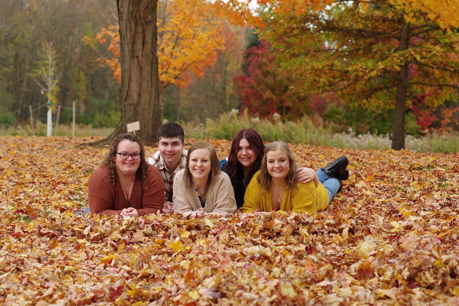 Group lying in fallen autumn leaves during outdoor photo session.