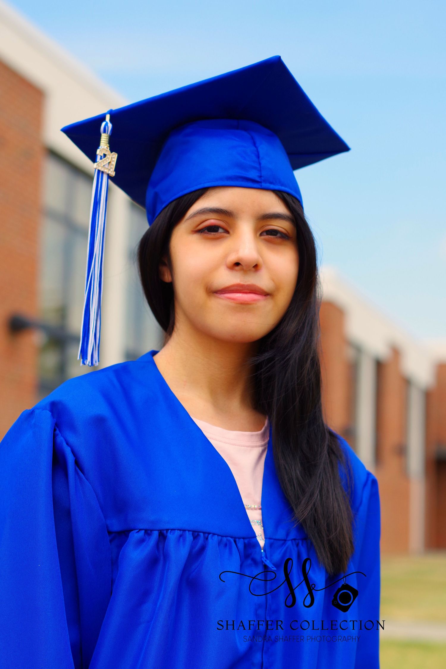 Graduate wearing bright blue academic regalia poses with tassel against brick building.