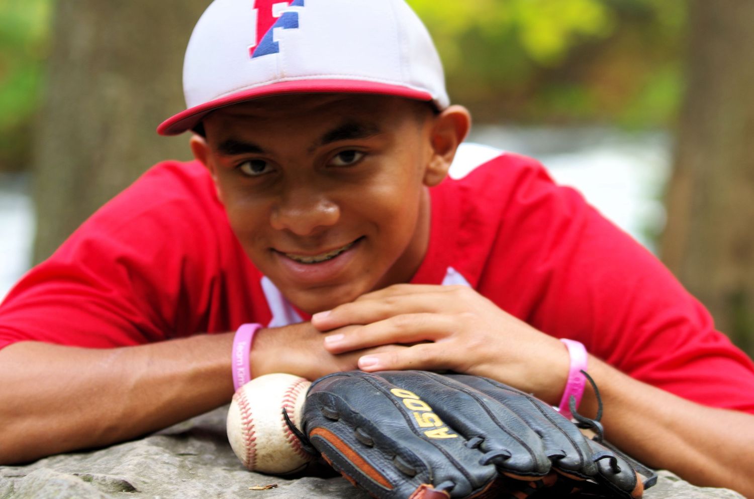 Baseball player with red cap rests next to baseball glove on stone surface.
