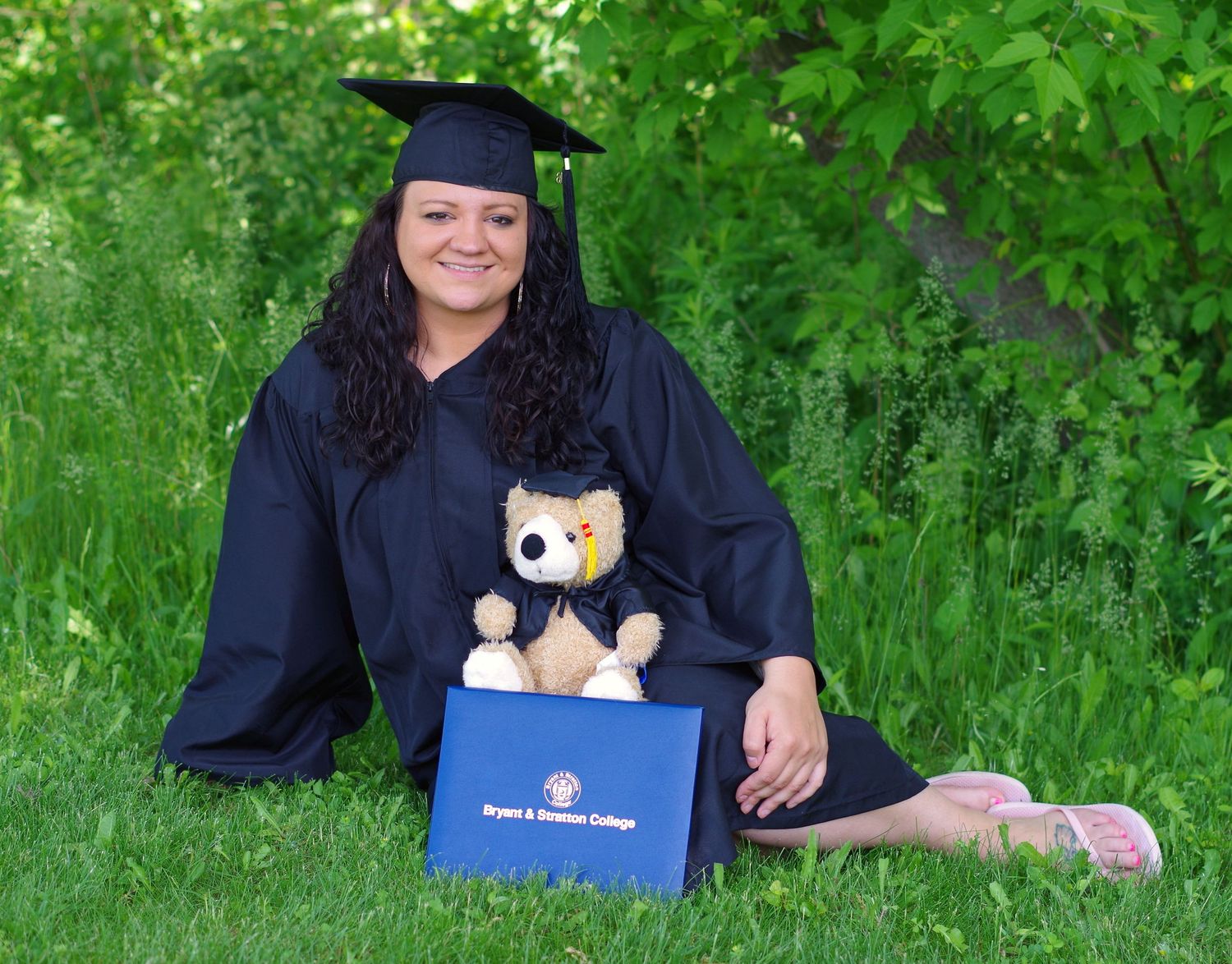 Graduate displays diploma and plush mascot during outdoor photo session.