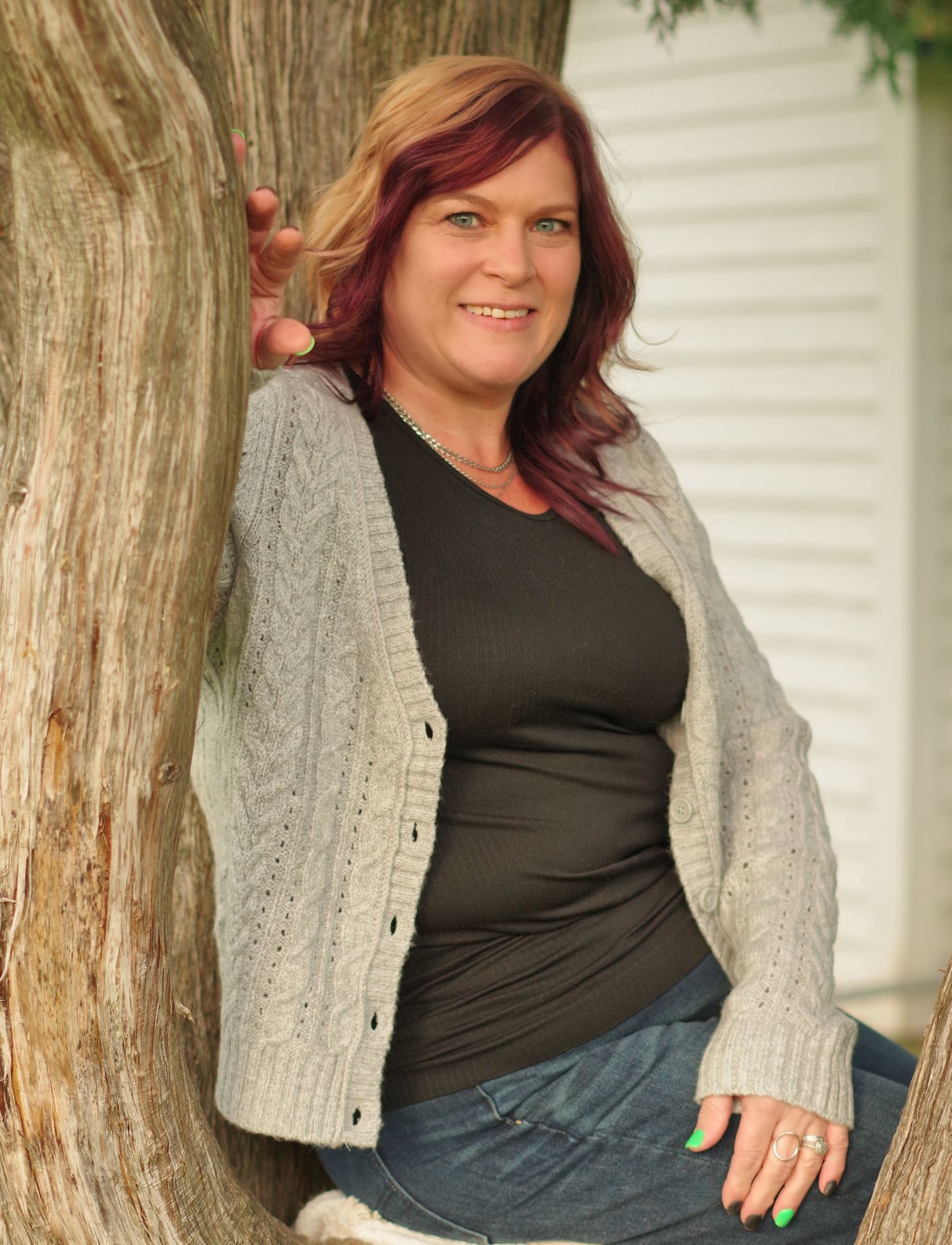Casual portrait against tree wearing gray cardigan and dark top in natural lighting.