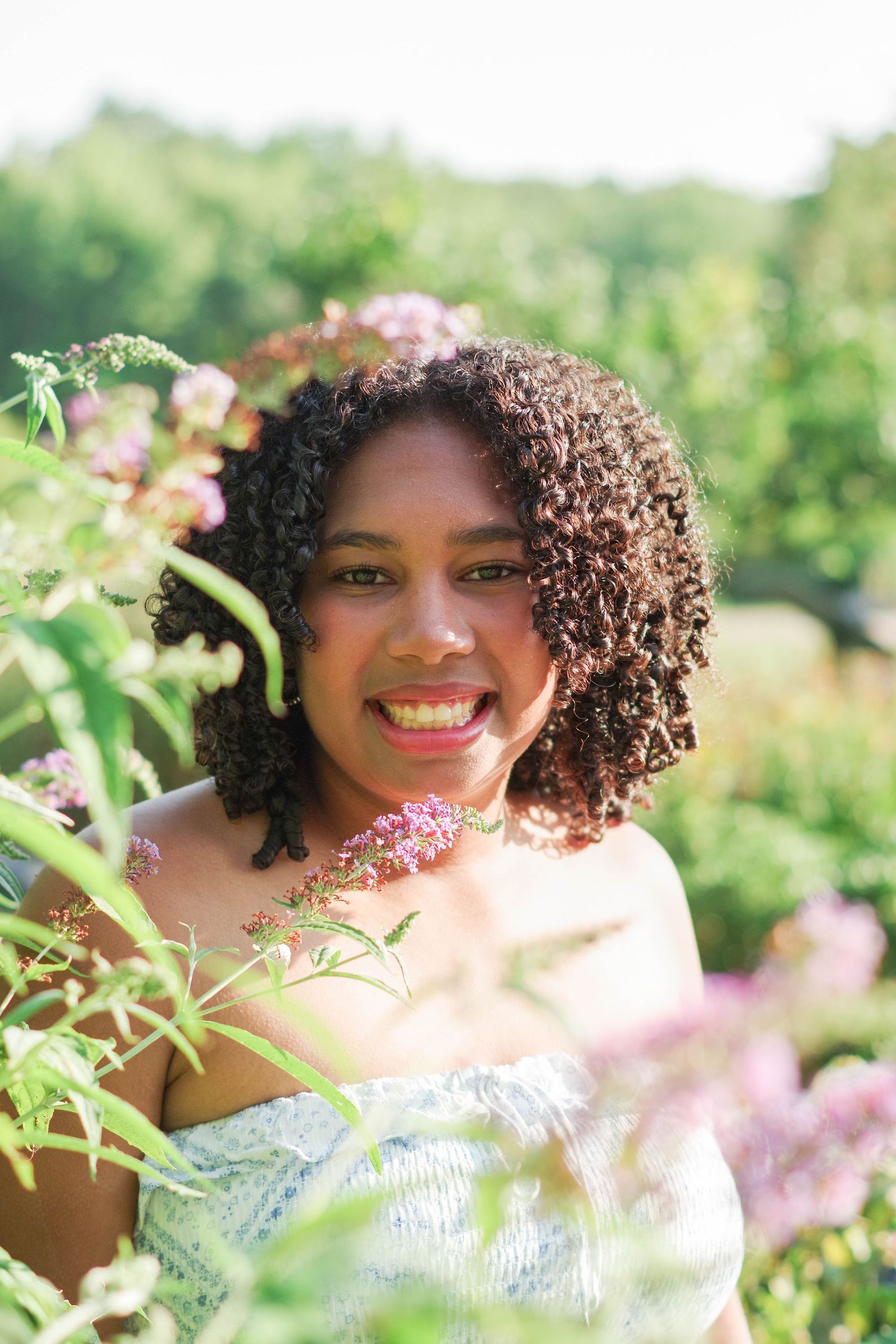 Smiling silhouette enjoying a sunny day outdoors surrounded by pink flowers and green foliage.