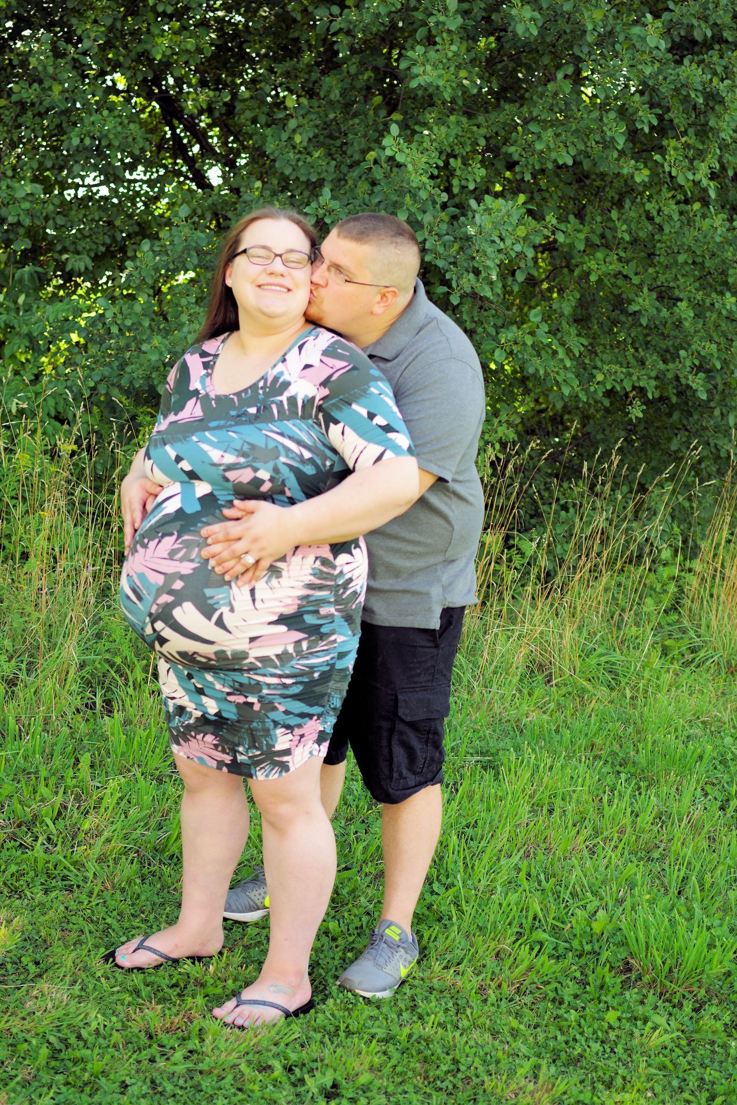 A couple embraces outdoors in a garden setting with green foliage in the background.