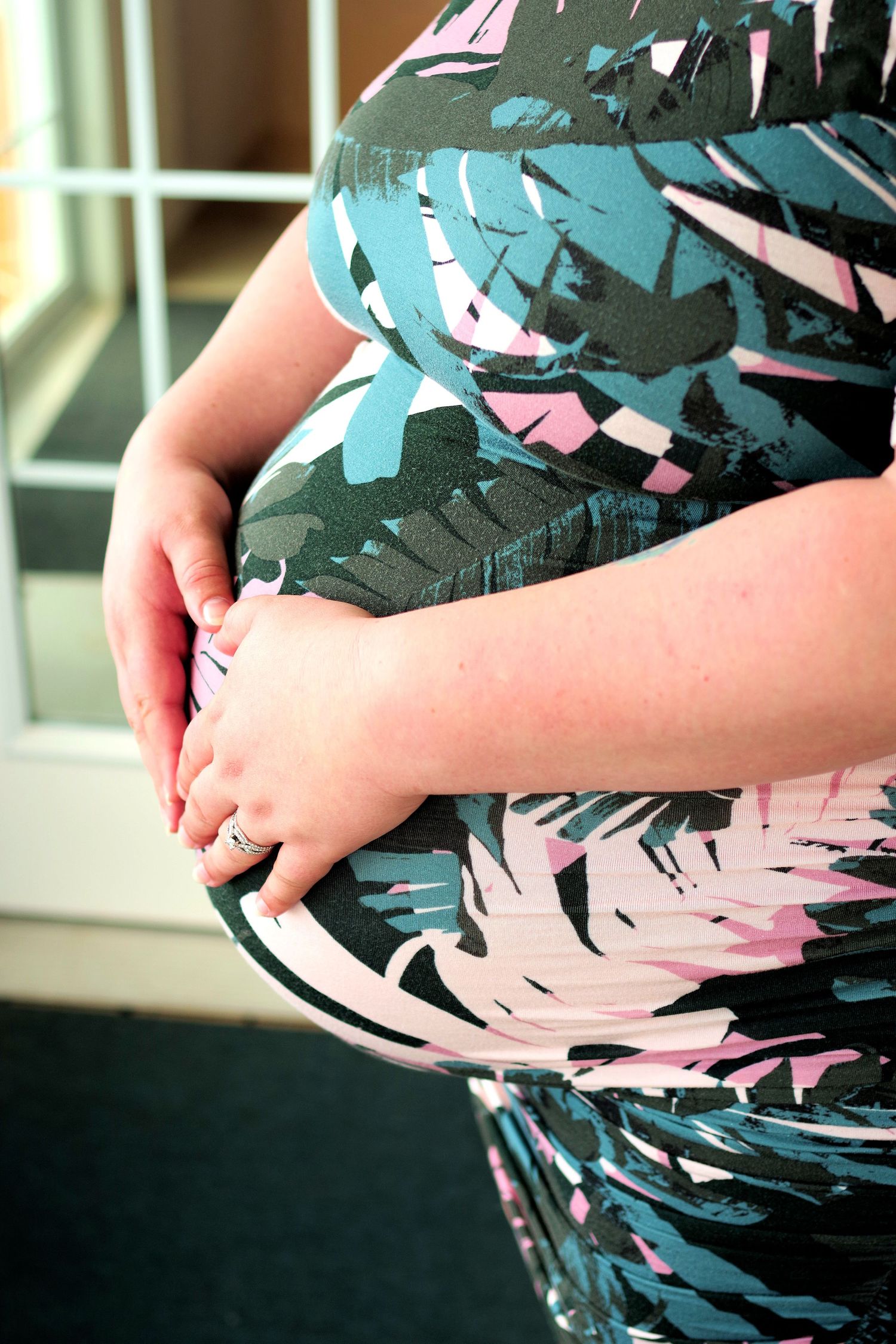 Close up of pregnant belly in teal and pink tropical print dress.
