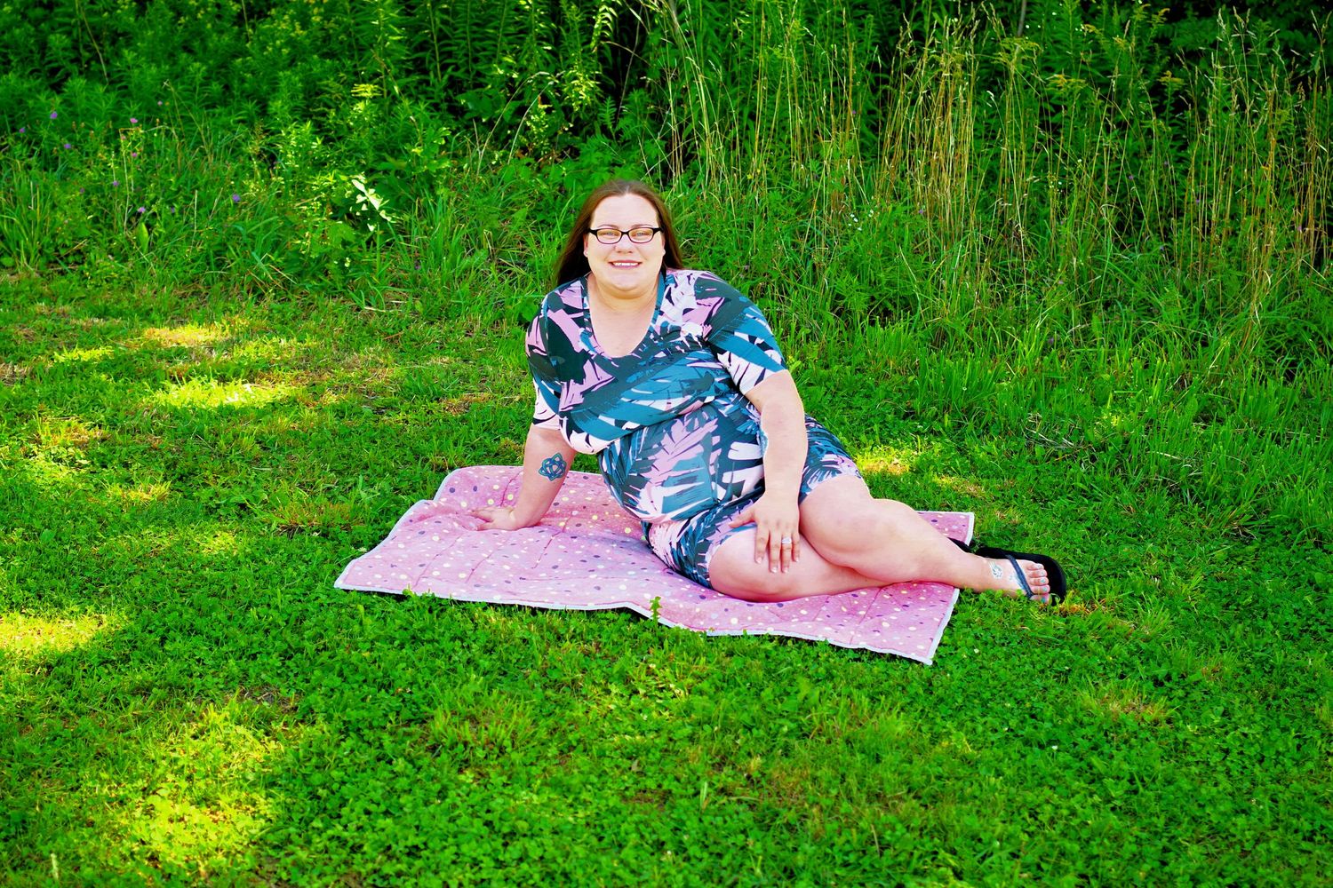 Maternity photo session on pink blanket in sunny green grass.