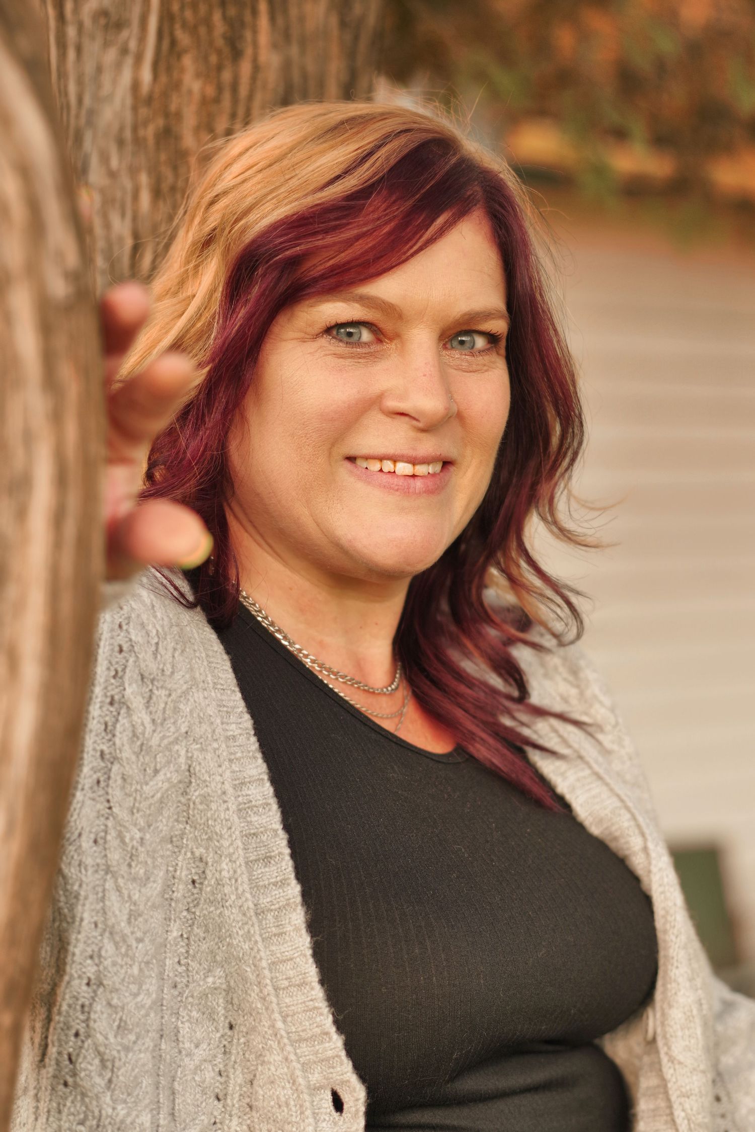 Portrait in autumn lighting showing casual style with cable knit cardigan and dark top against tree backdrop.