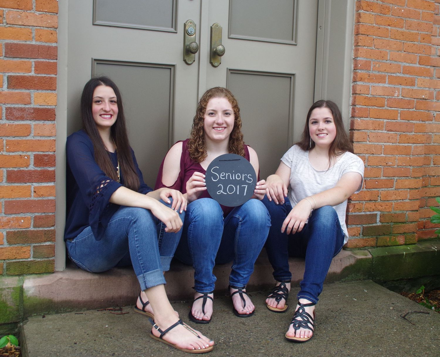 Friends sitting together on concrete steps in front of grey door wearing casual outfits.