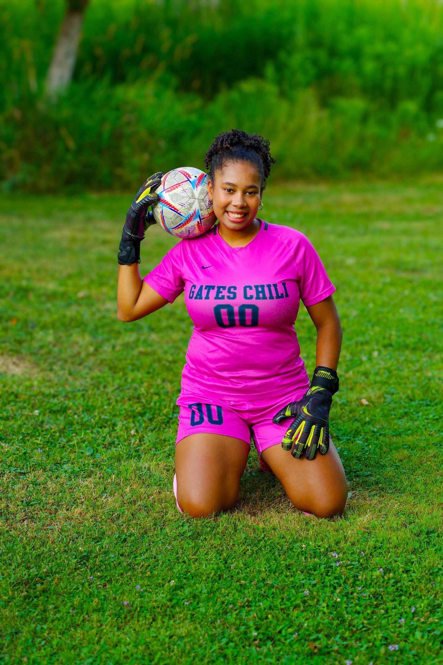 Soccer goalkeeper in pink jersey crouching on grass field while holding ball during action sequence.
