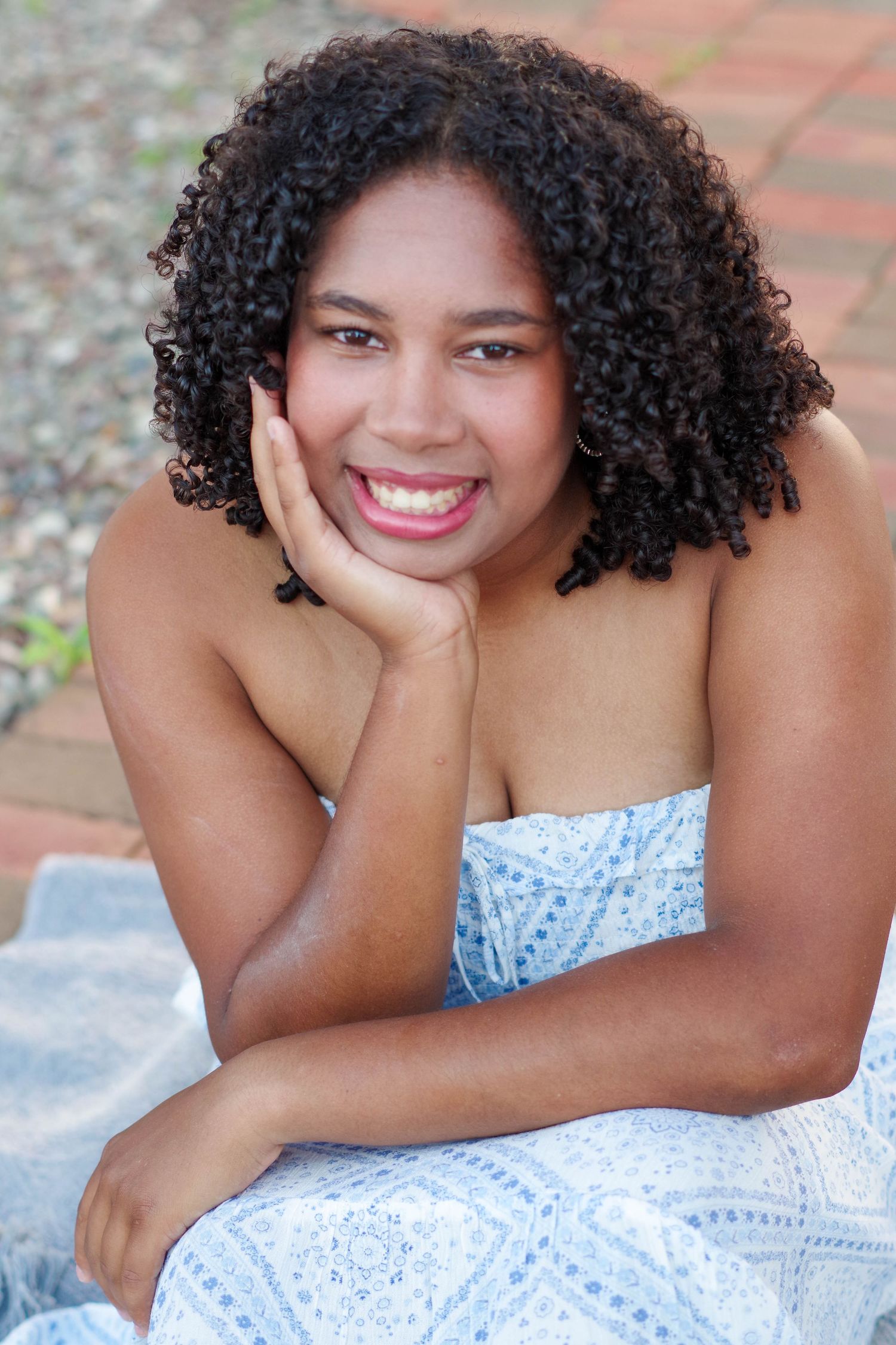 Outdoor portrait in a white lace dress showing bright smile and natural curly hair against a light background.