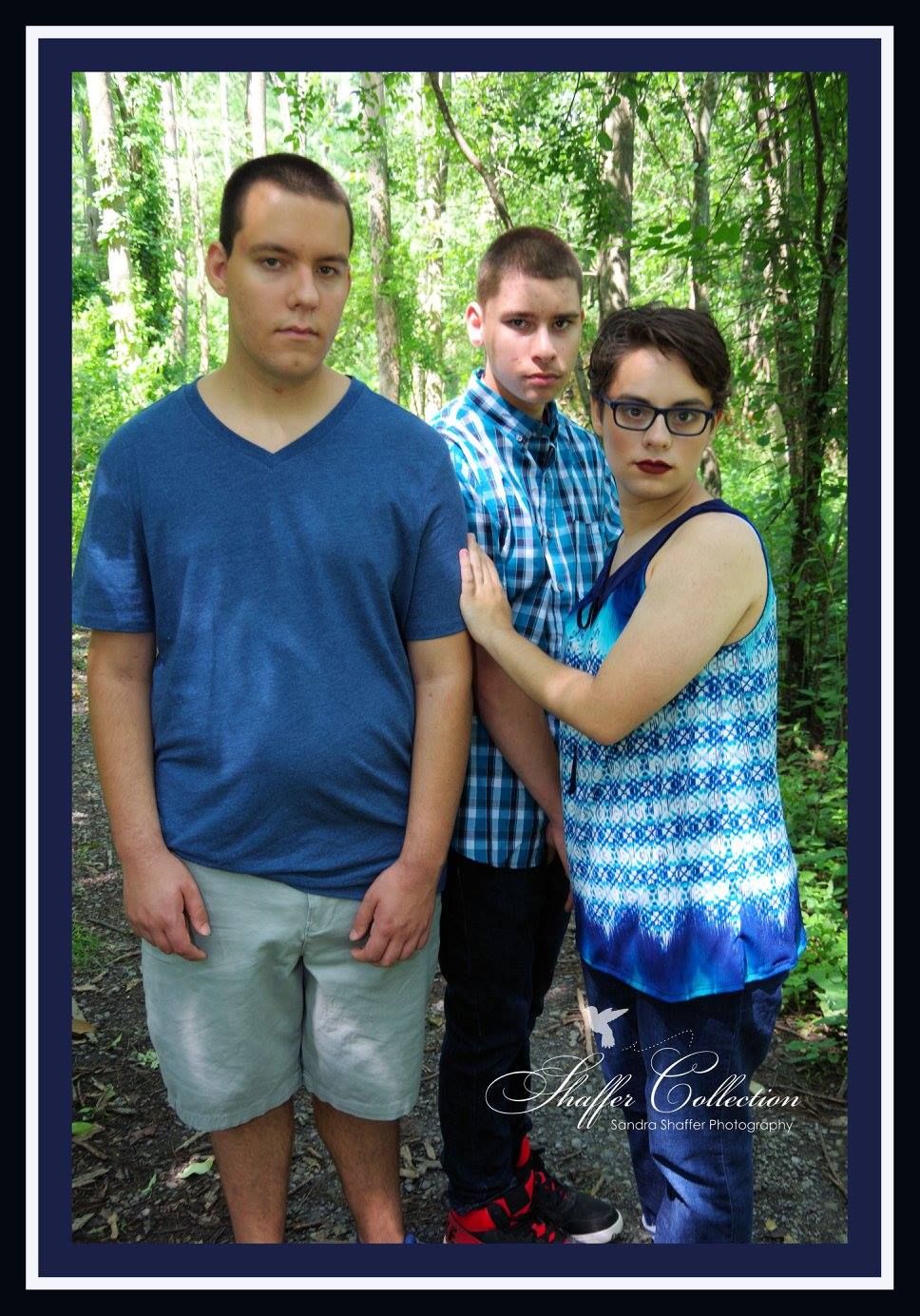 Three people pose casually in front of a wooded background wearing blue and patterned clothing.