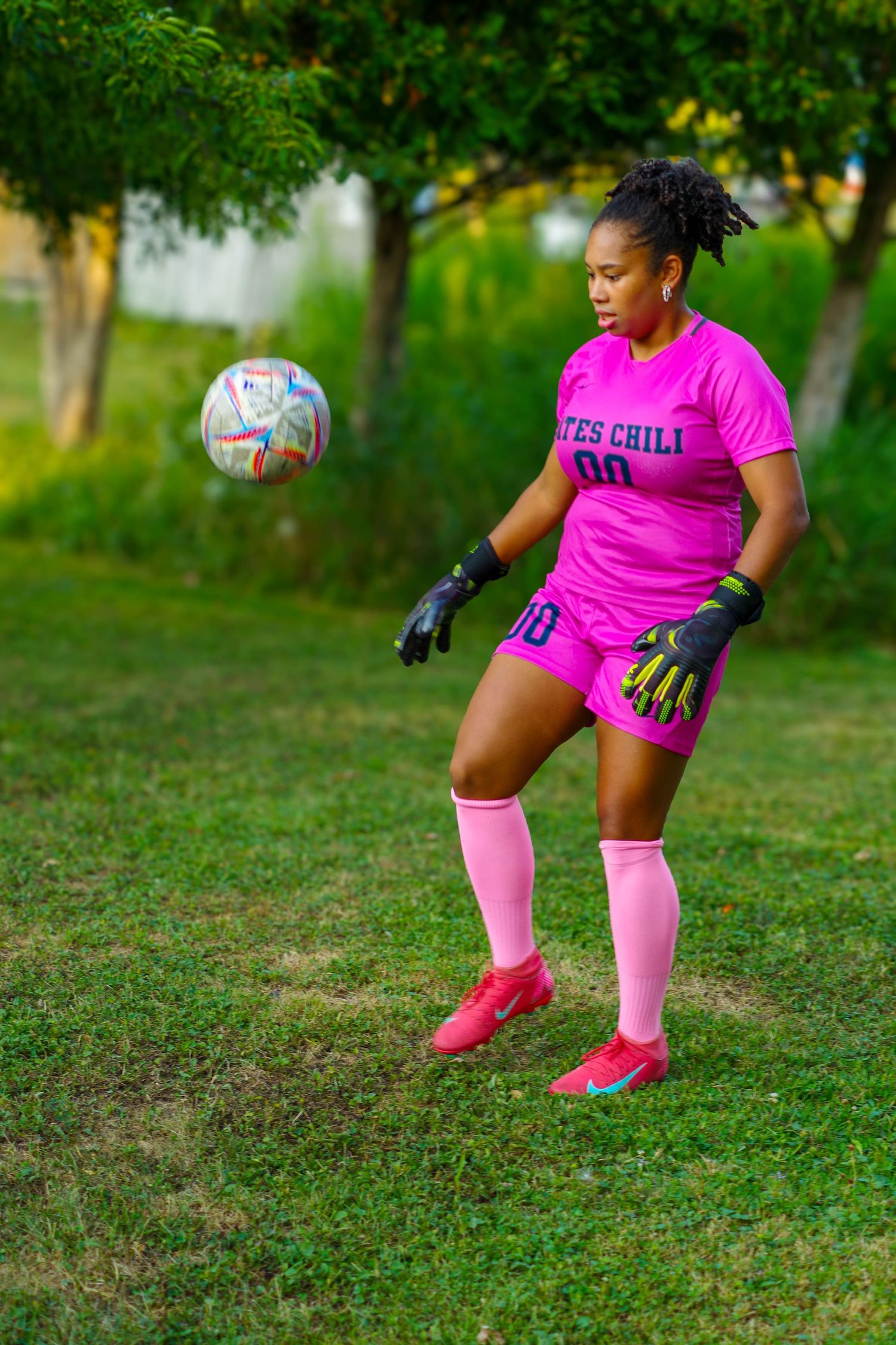 Soccer player in pink uniform and knee socks crouches low while practicing defensive moves on grass field.