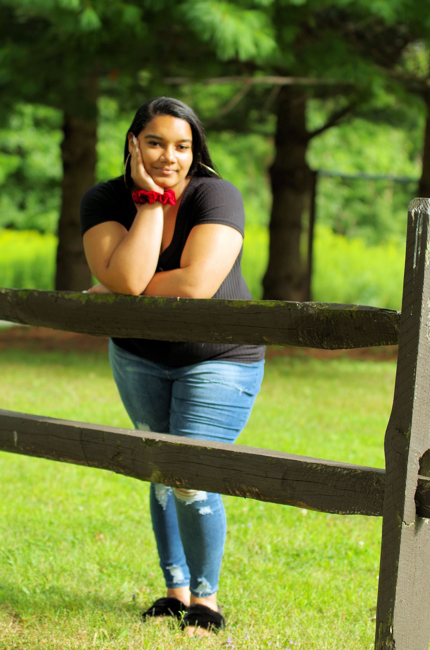 A cheerful outdoor portrait leaning on a rustic wooden fence in a park setting.
