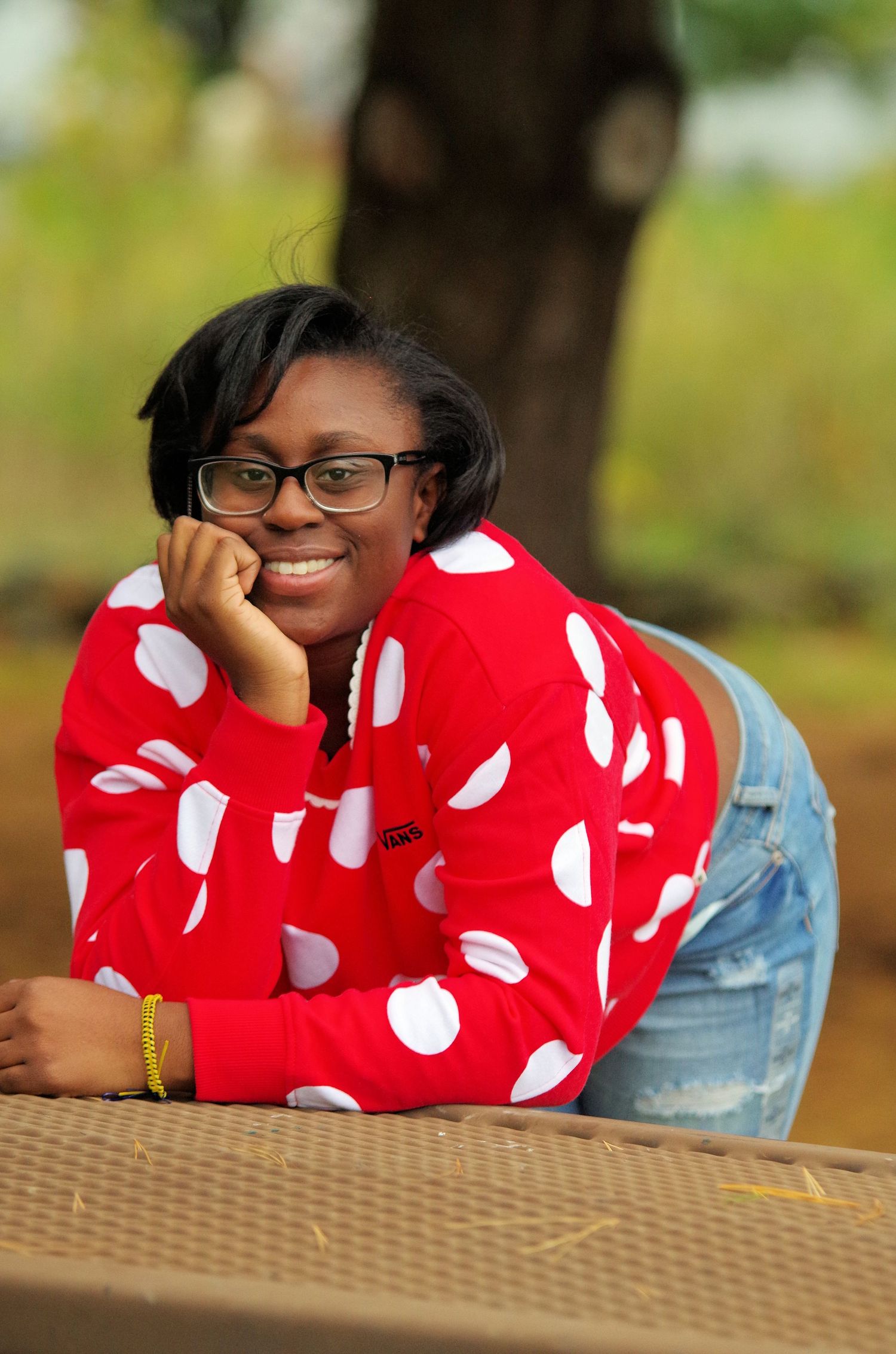 Portrait in red polka dot sweater leaning on outdoor table.