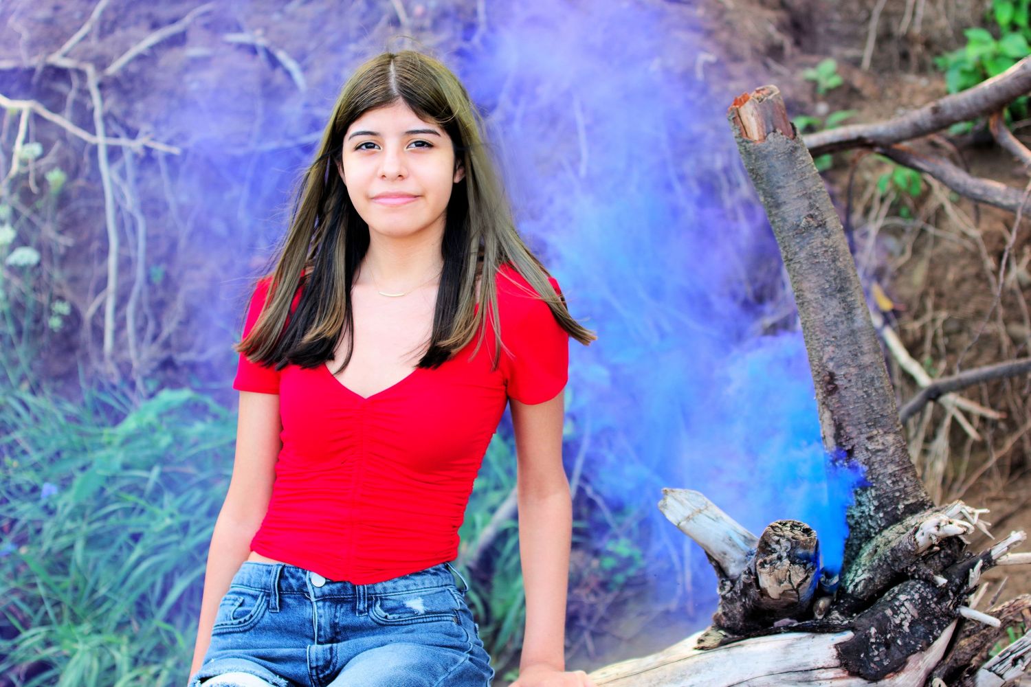 Artistic portrait with purple smoke effect wearing red top near fallen logs.
