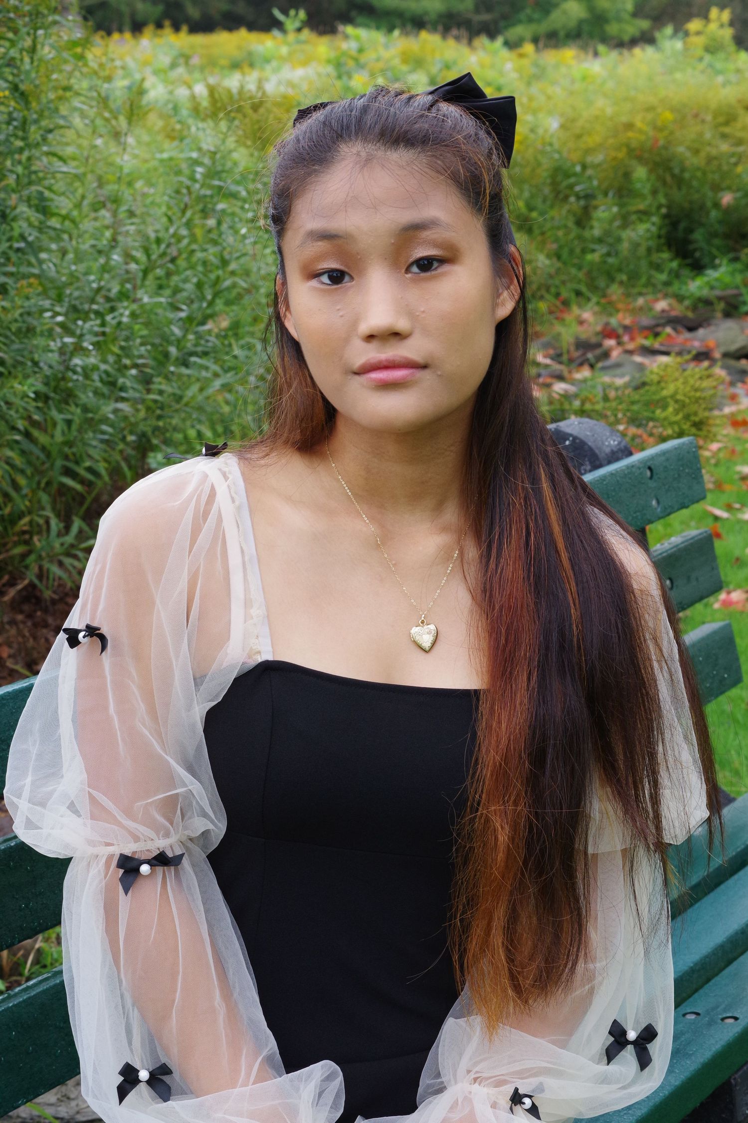 Portrait in garden setting wearing black dress with sheer puff sleeves and delicate necklace.