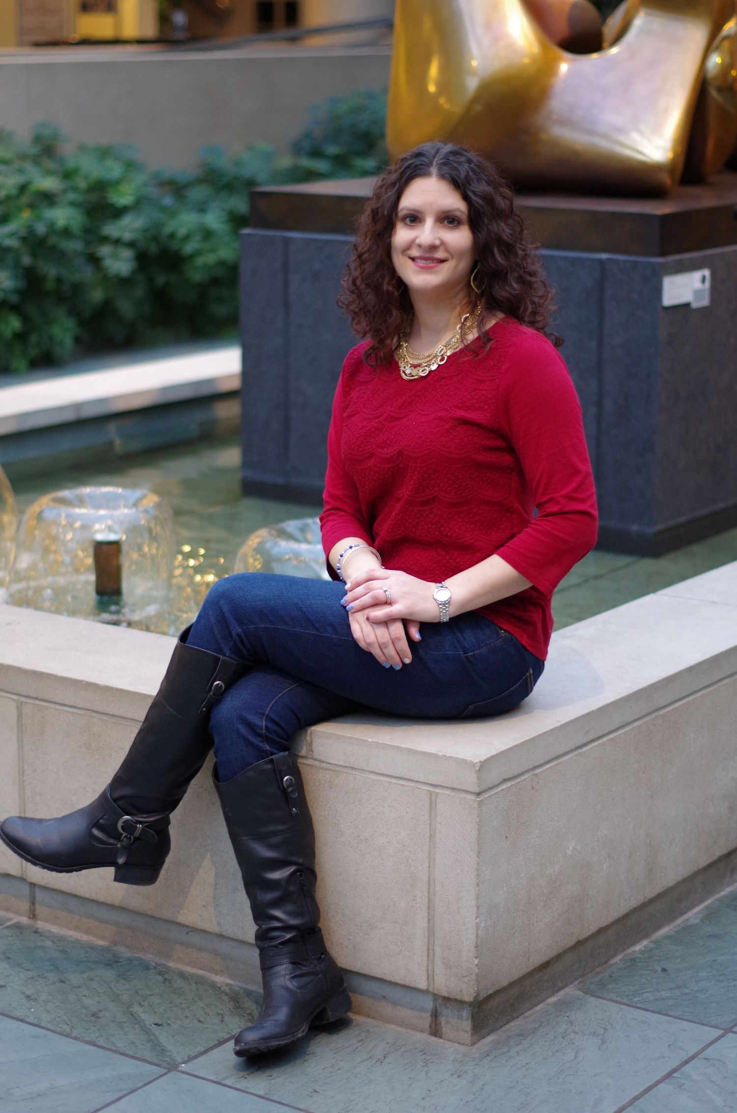 A person in red sweater and boots sits on stone ledge near a water feature.