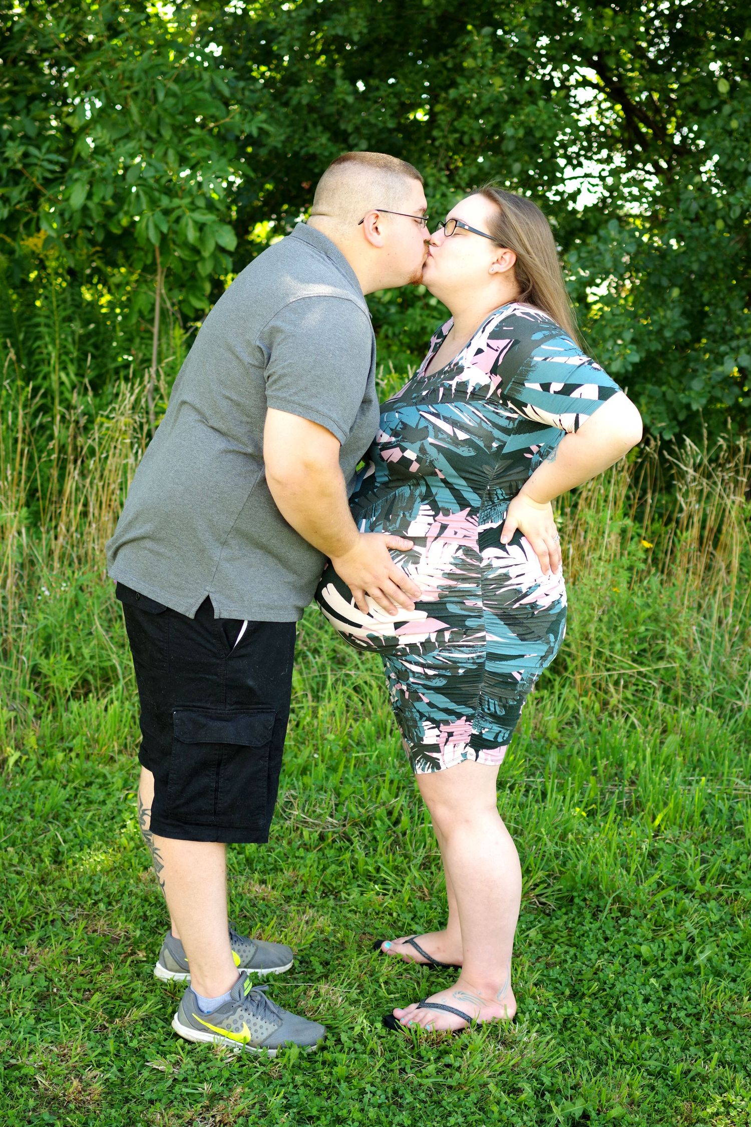 A playful outdoor portrait of a couple sharing a kiss against a green foliage background.