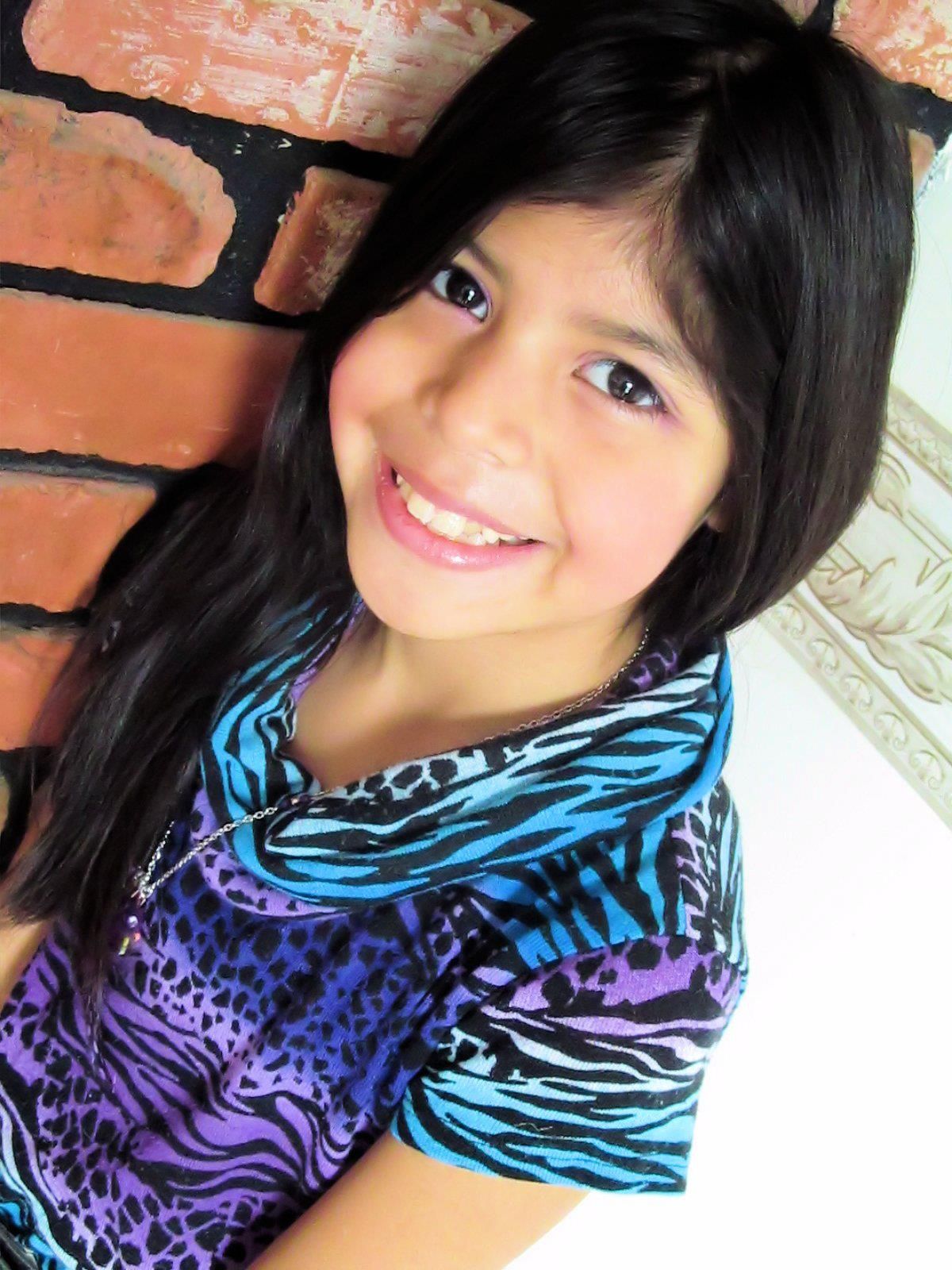 A person in a colorful zebra print top poses against an orange brick wall.