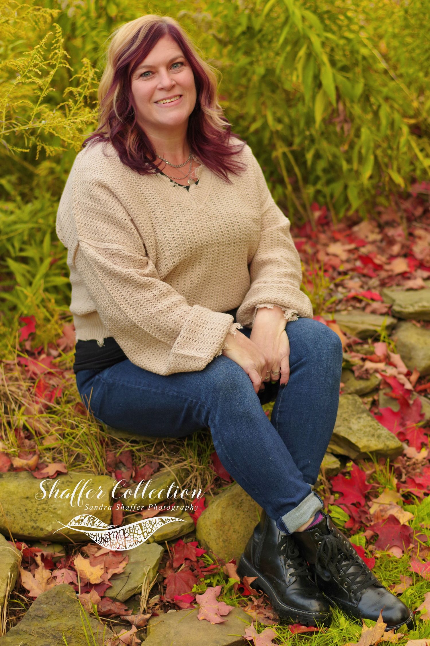 Outdoor fall portrait with beige sweater sitting among colorful autumn leaves.