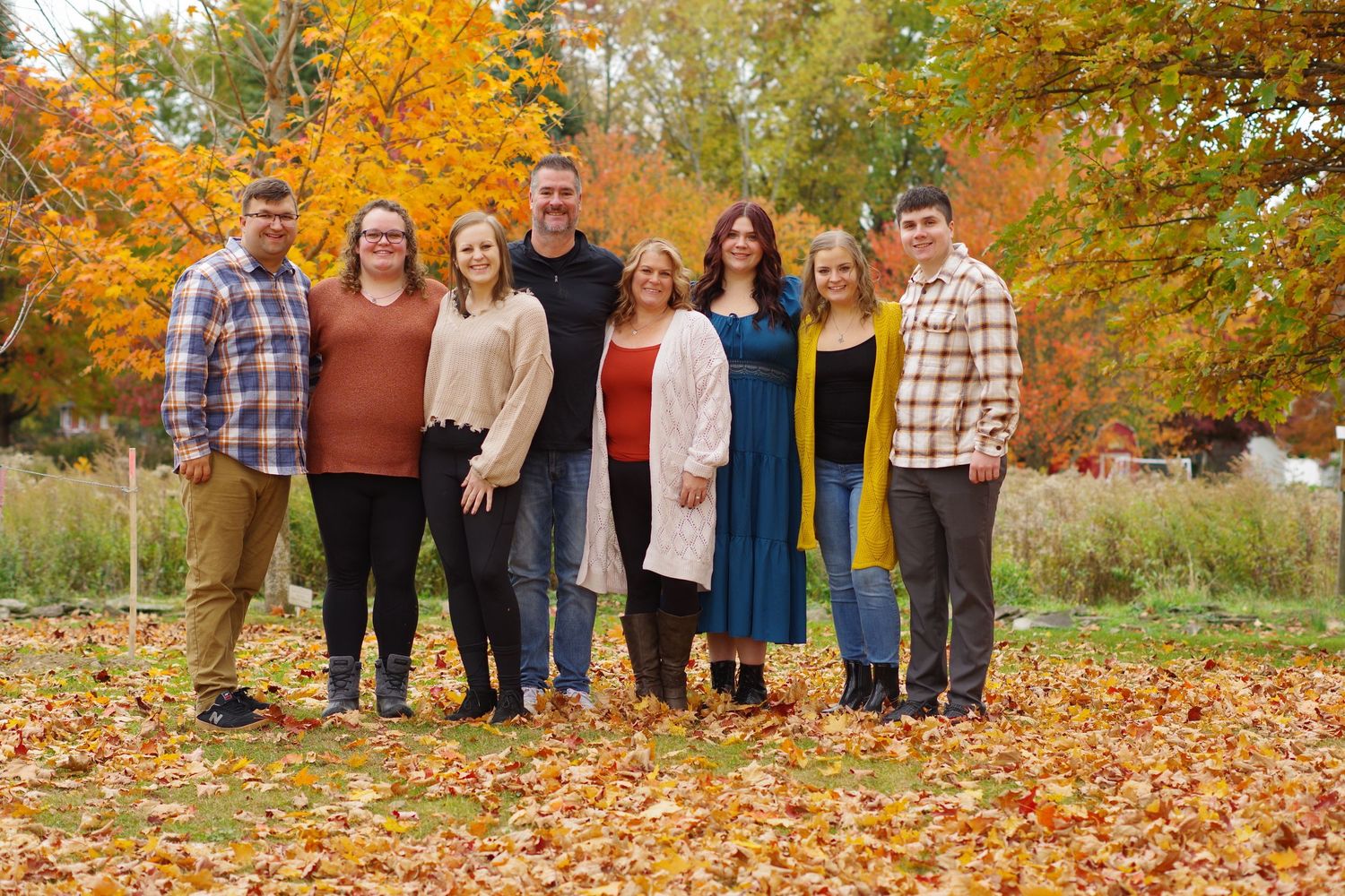 Group standing together on fallen leaves with autumn trees in background.