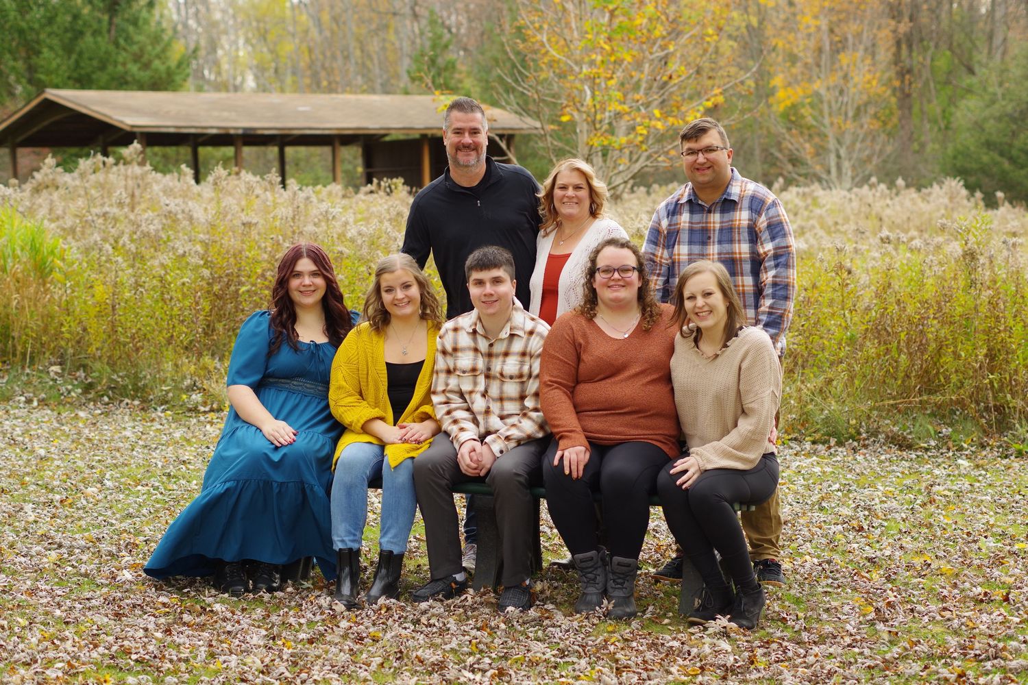 Large group sitting together on grass for outdoor autumn family photo.