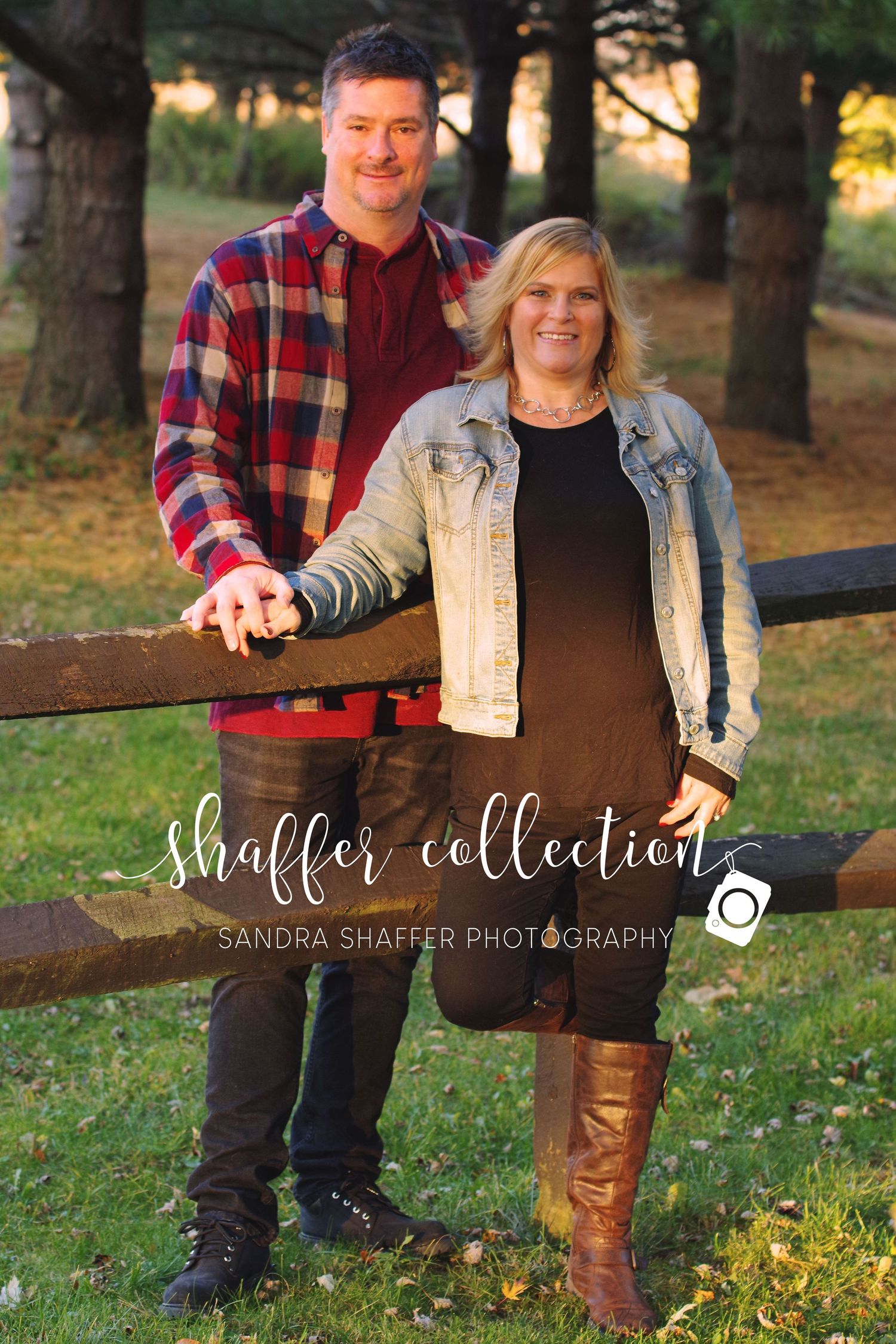 A couple poses by a wooden fence during autumn, wearing casual outdoor attire.