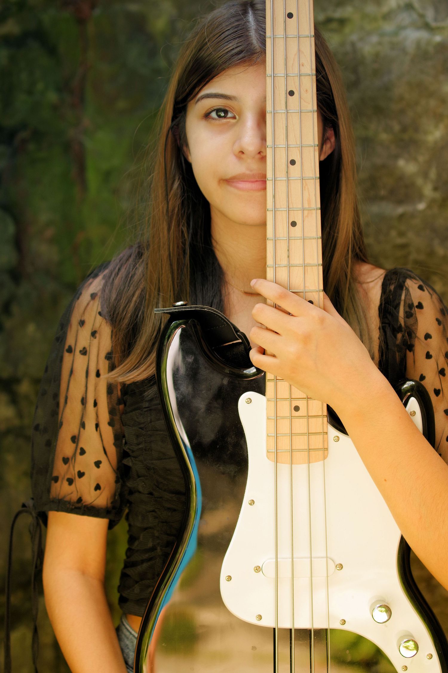 Person posing with white bass guitar against natural outdoor background.