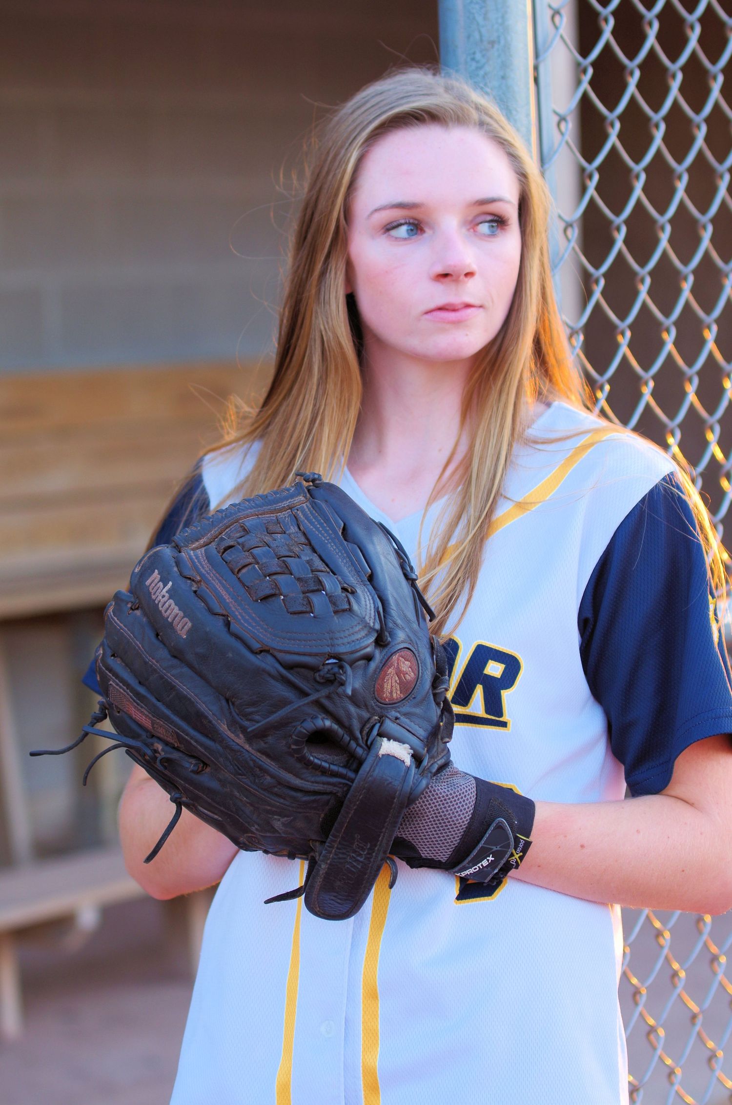 Athlete in Victor team uniform poses with baseball glove by chain link fence.