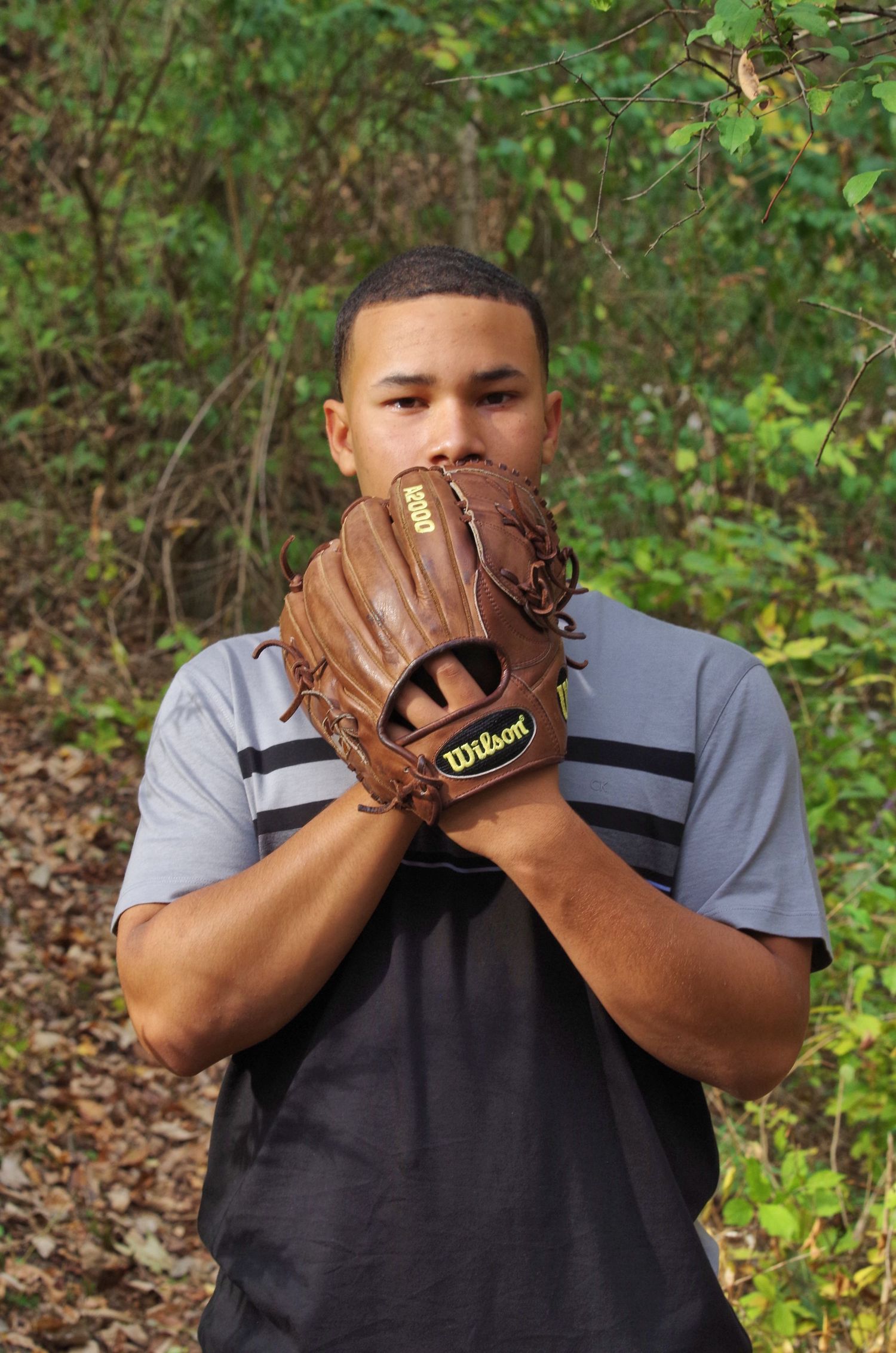 Baseball player holding up glove in defensive position against natural background.