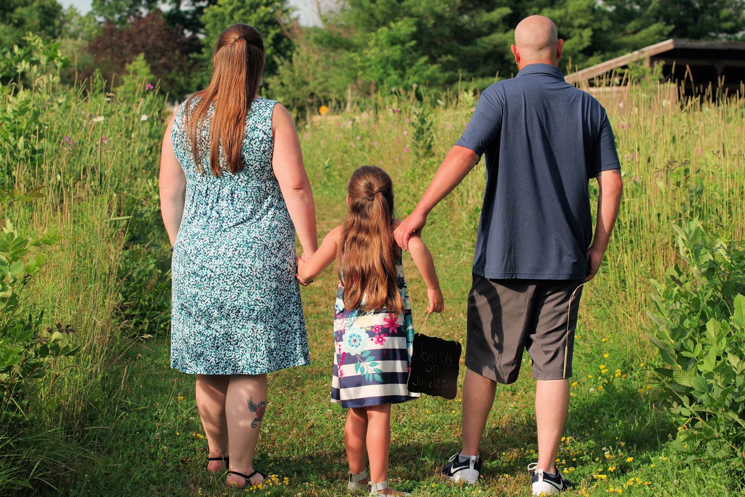 Family walks hand in hand through tall summer grass on nature trail.
