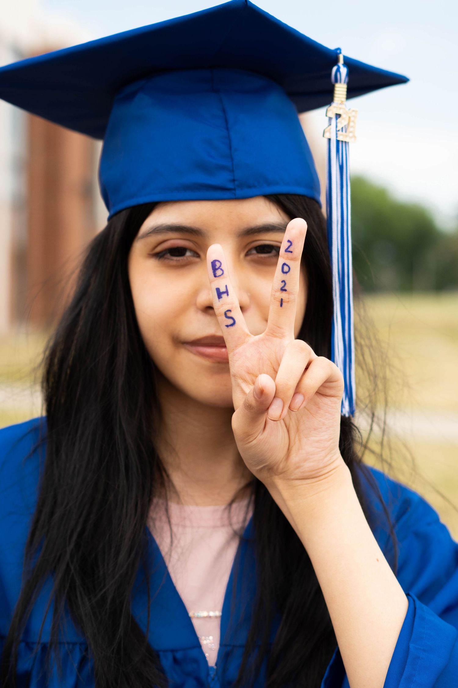 Graduate in blue cap and gown makes peace sign gesture during photo session.