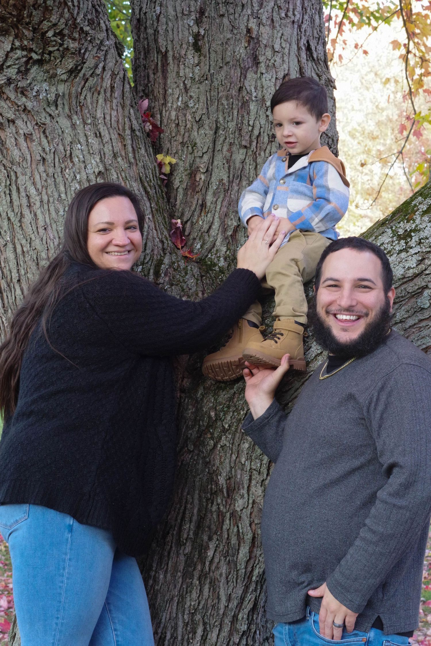 Family poses playfully by large tree trunk during outdoor photo session.