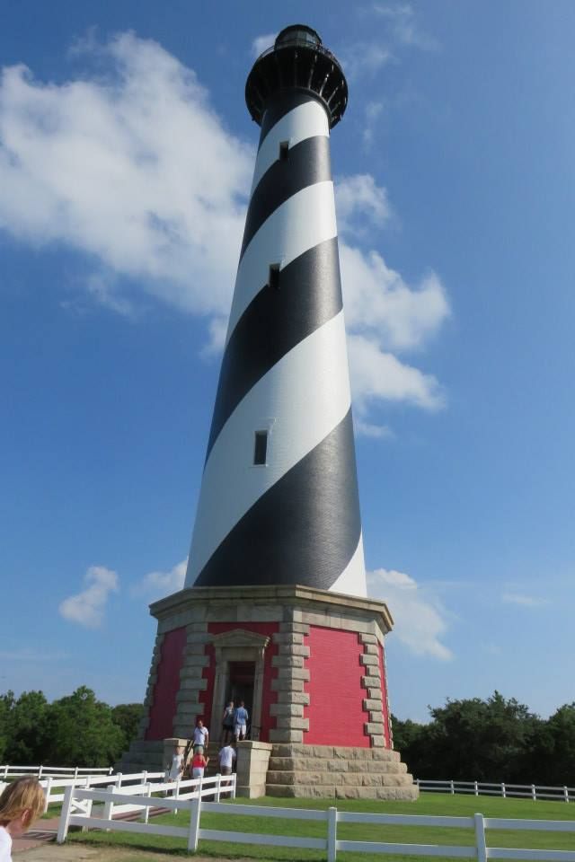 The Cape Hatteras lighthouse stands tall with its distinctive black and white spiral stripes against a blue sky.
