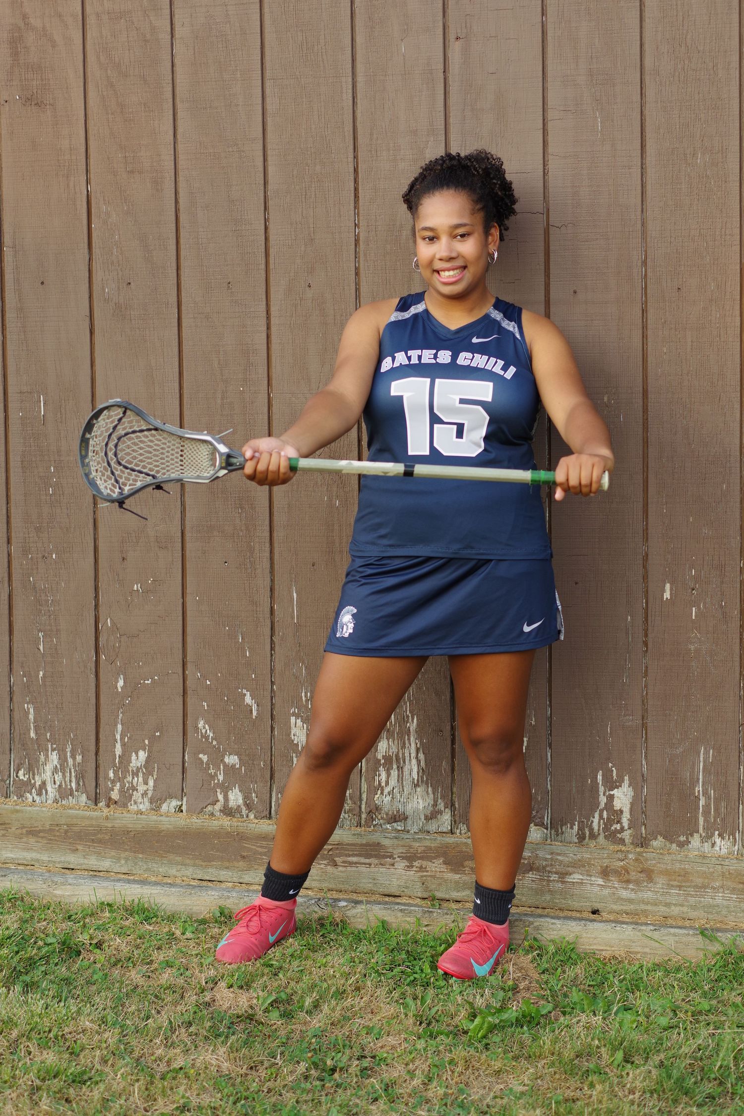 Athlete demonstrates lacrosse stance while wearing navy uniform against wooden backdrop.