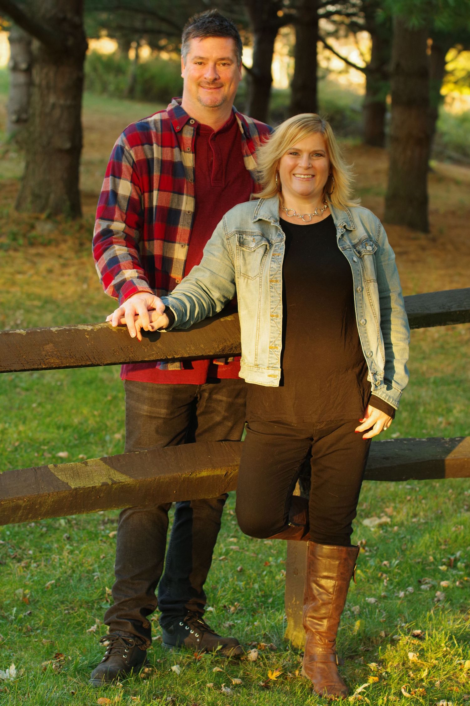 Couple in coordinated casual outfits standing by a wooden fence in an autumn setting.