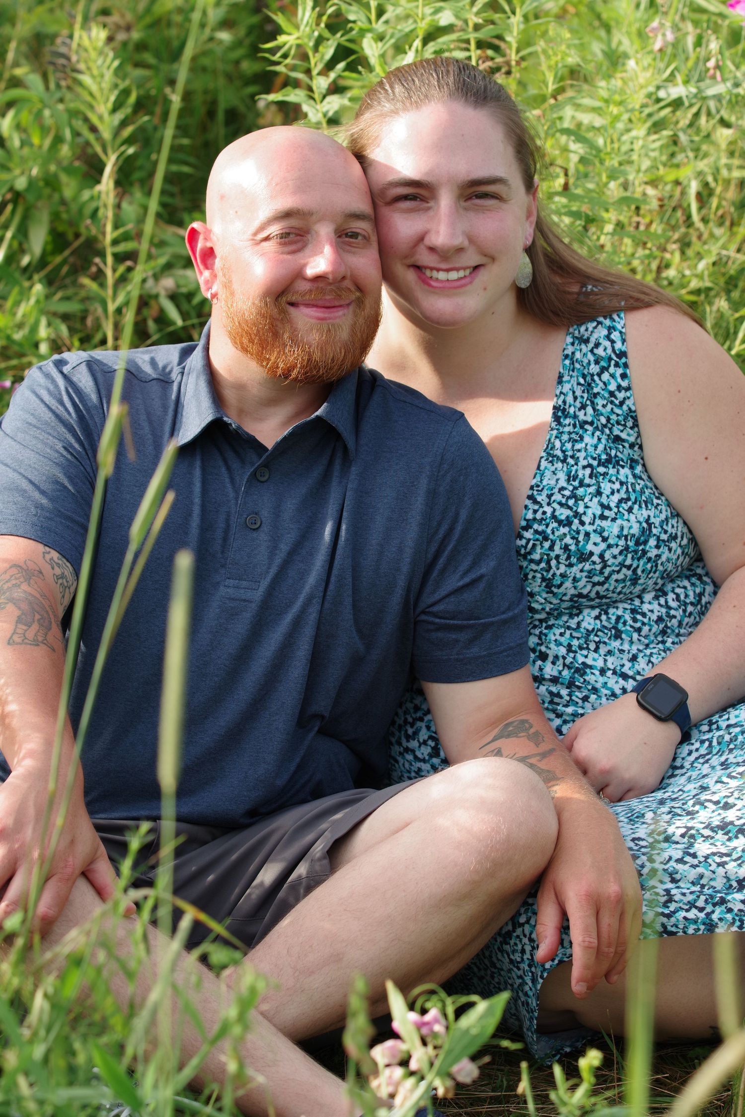 A summer couple's portrait surrounded by tall green plants and natural sunlight.