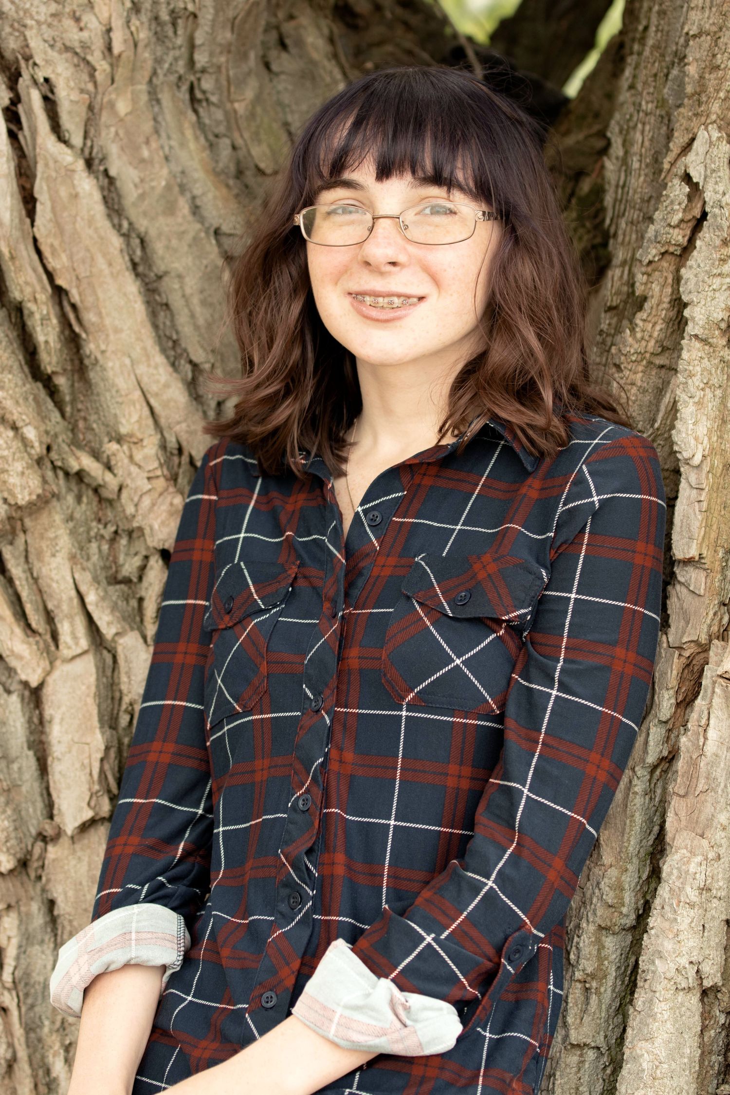 Natural portrait between tree trunks wearing plaid flannel shirt.