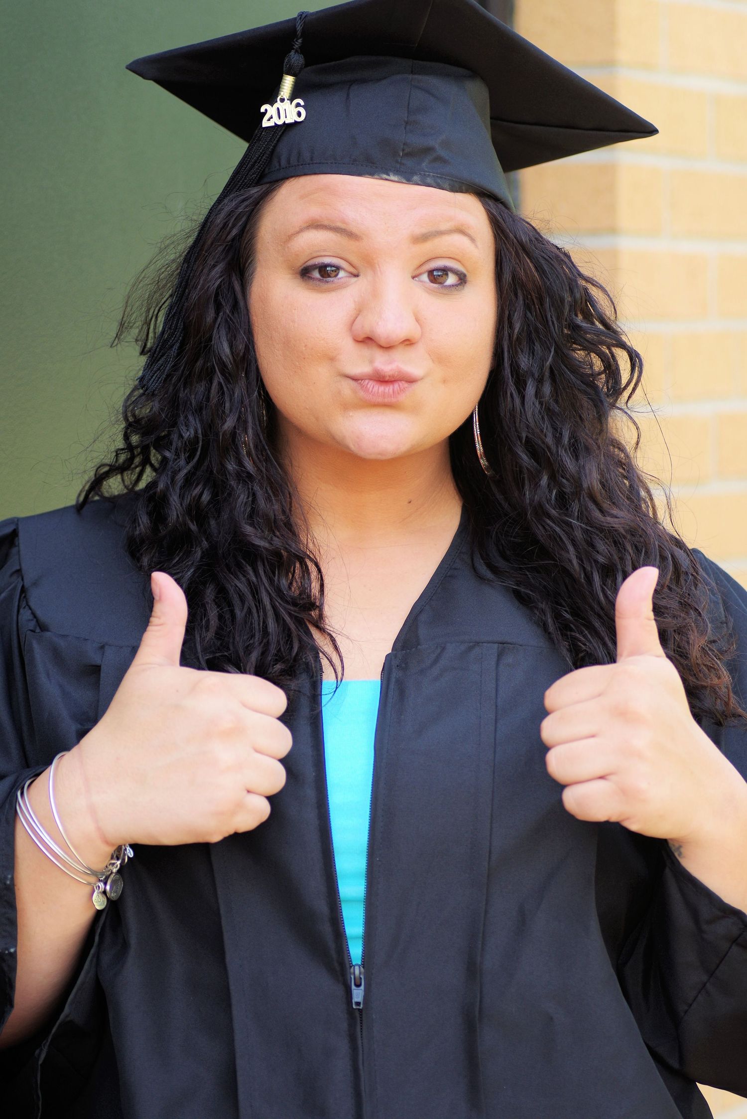 Graduate in black academic regalia gives double thumbs up with cheerful expression.