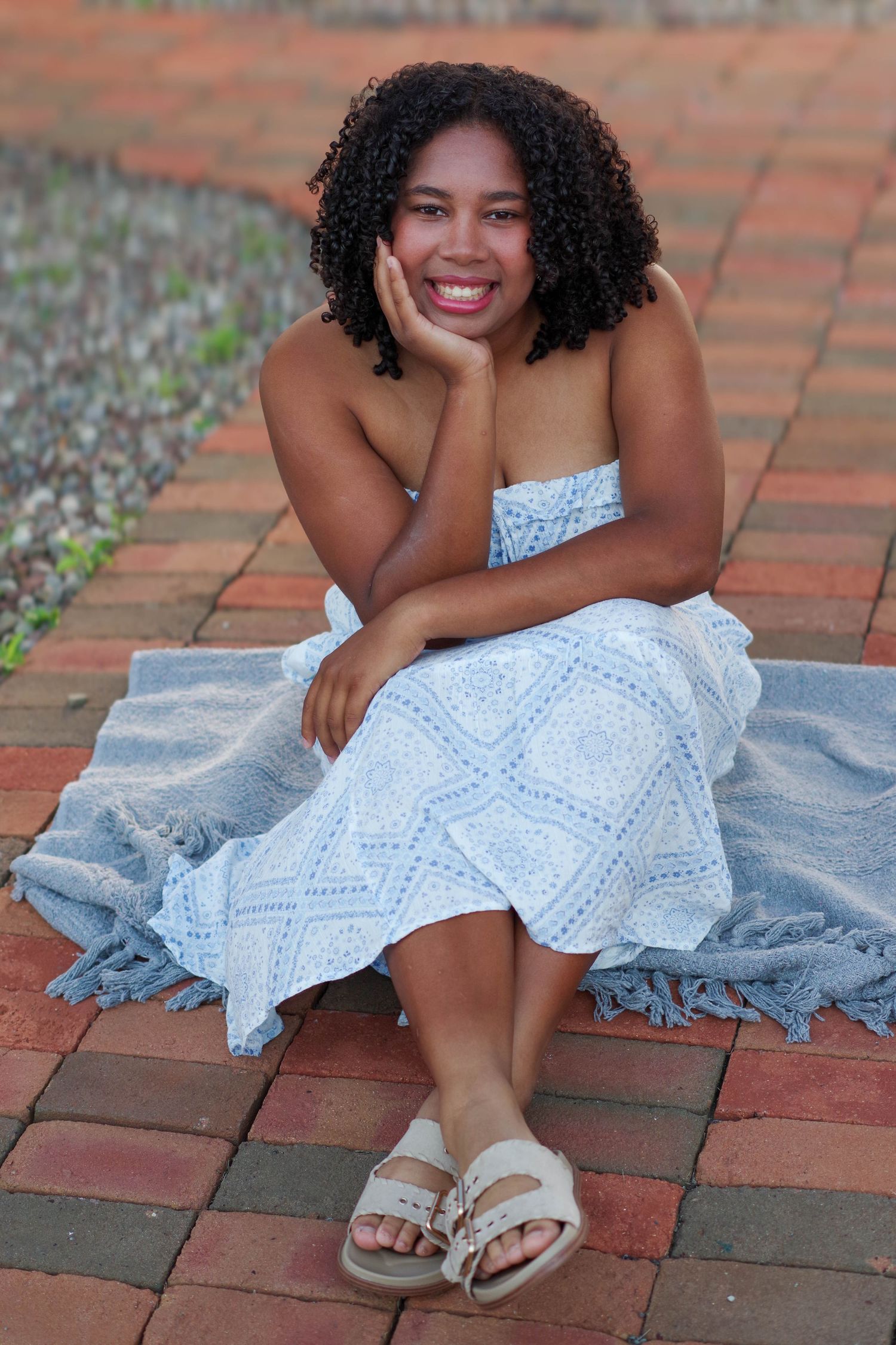 Portrait of someone in white dress sitting on brick steps with natural curls.