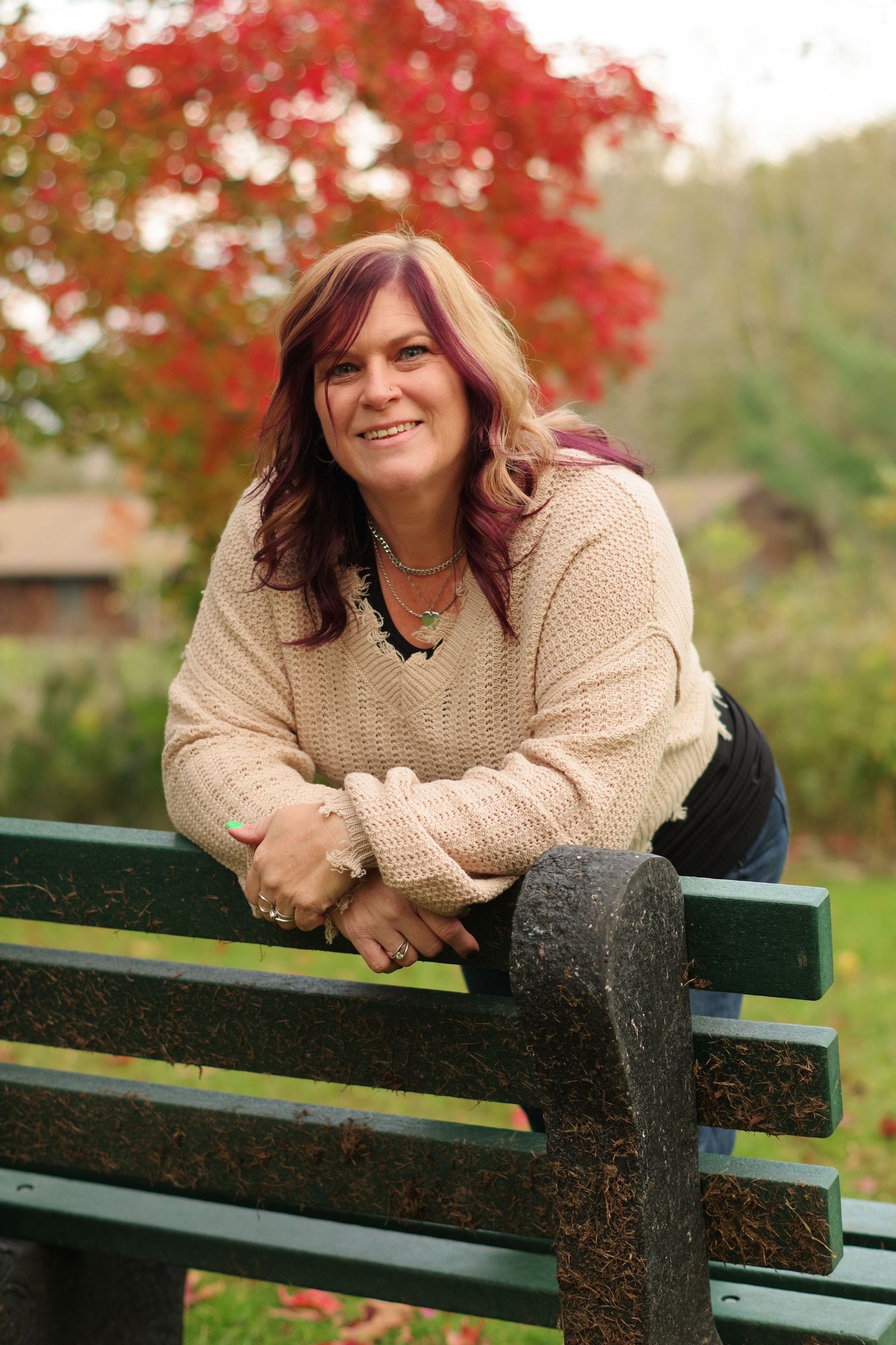 Cozy outdoor portrait against bright red maple trees with person wearing beige knit sweater.
