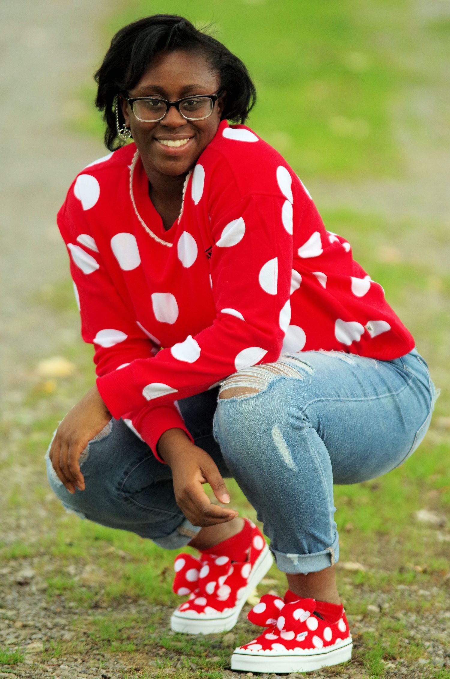 Person in red and white polka dot sweater and jeans crouching on grass.