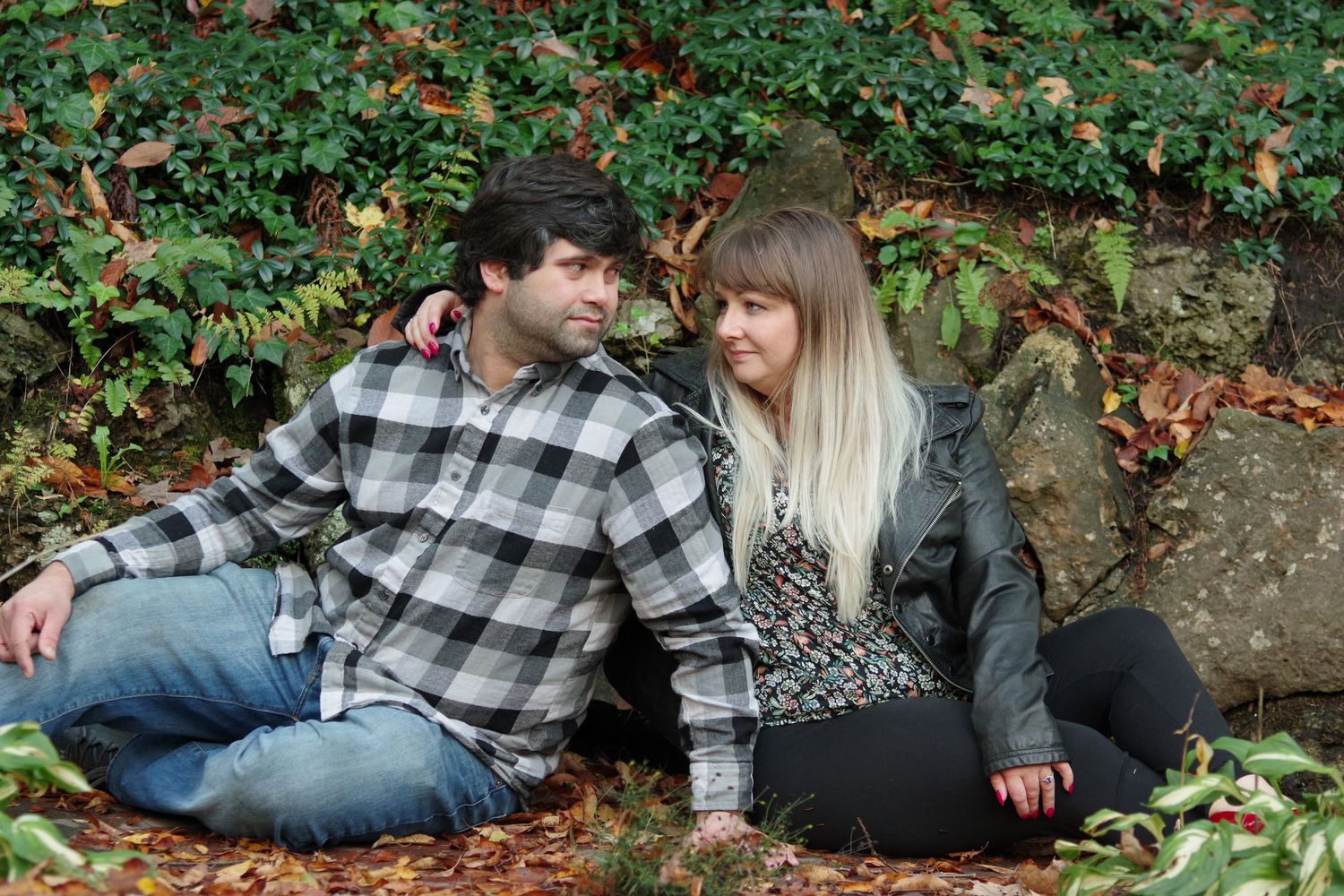 Couple in casual wear sitting together among autumn leaves and vines.