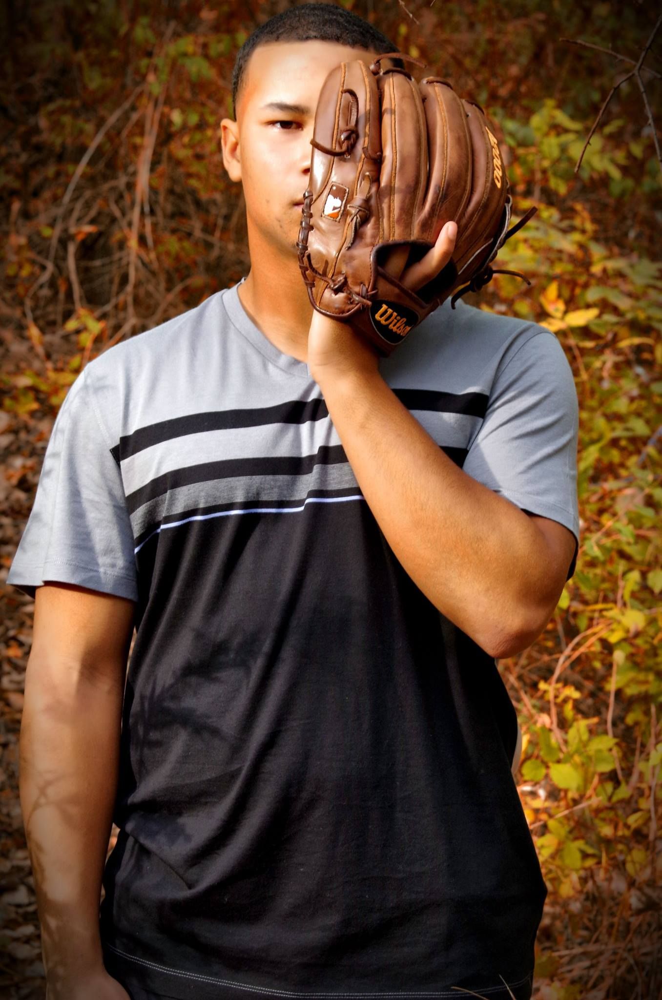 Player wearing striped jersey holds up baseball glove in outdoor setting.