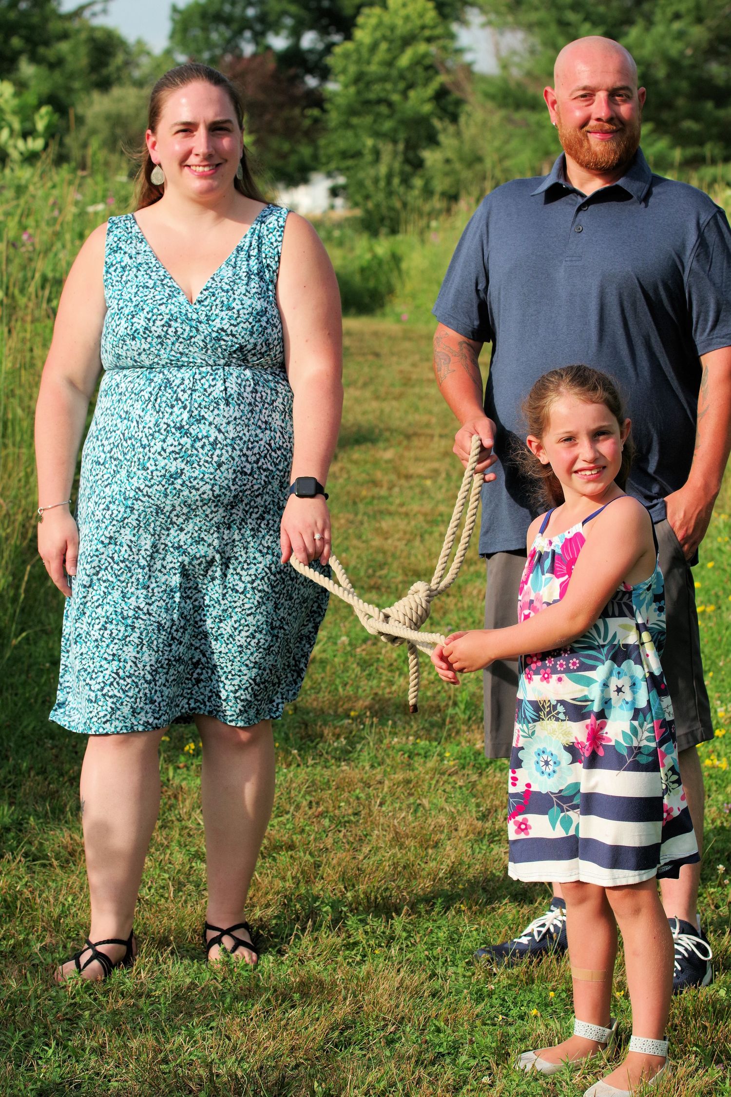 Family poses together outdoors with one member holding up a large deer antler in a grassy field.